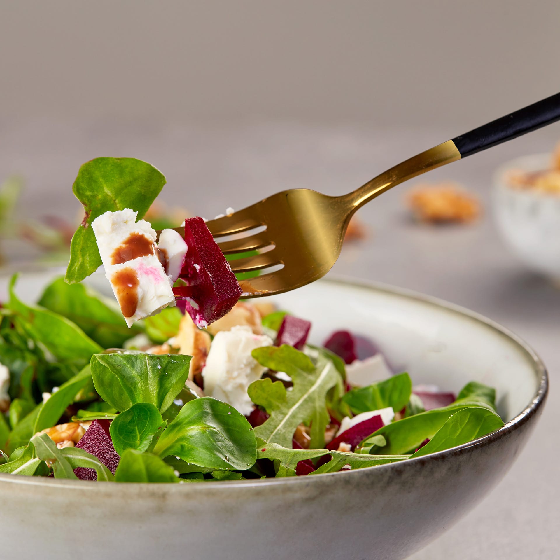 Świeża sałatka z burakiem, pokruszonym serem feta i mieszanymi ziołami uniesiona jest widelcem, prezentując zdrowe i kolorowe danie w ceramicznej misce na fakturowanej powierzchni.