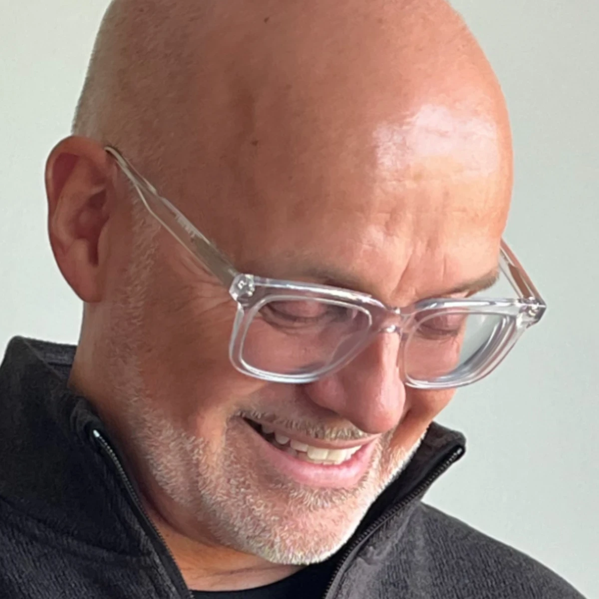 Close-up portrait of Stéphane Paquet smiling while looking down, wearing clear glasses and a dark sweater.