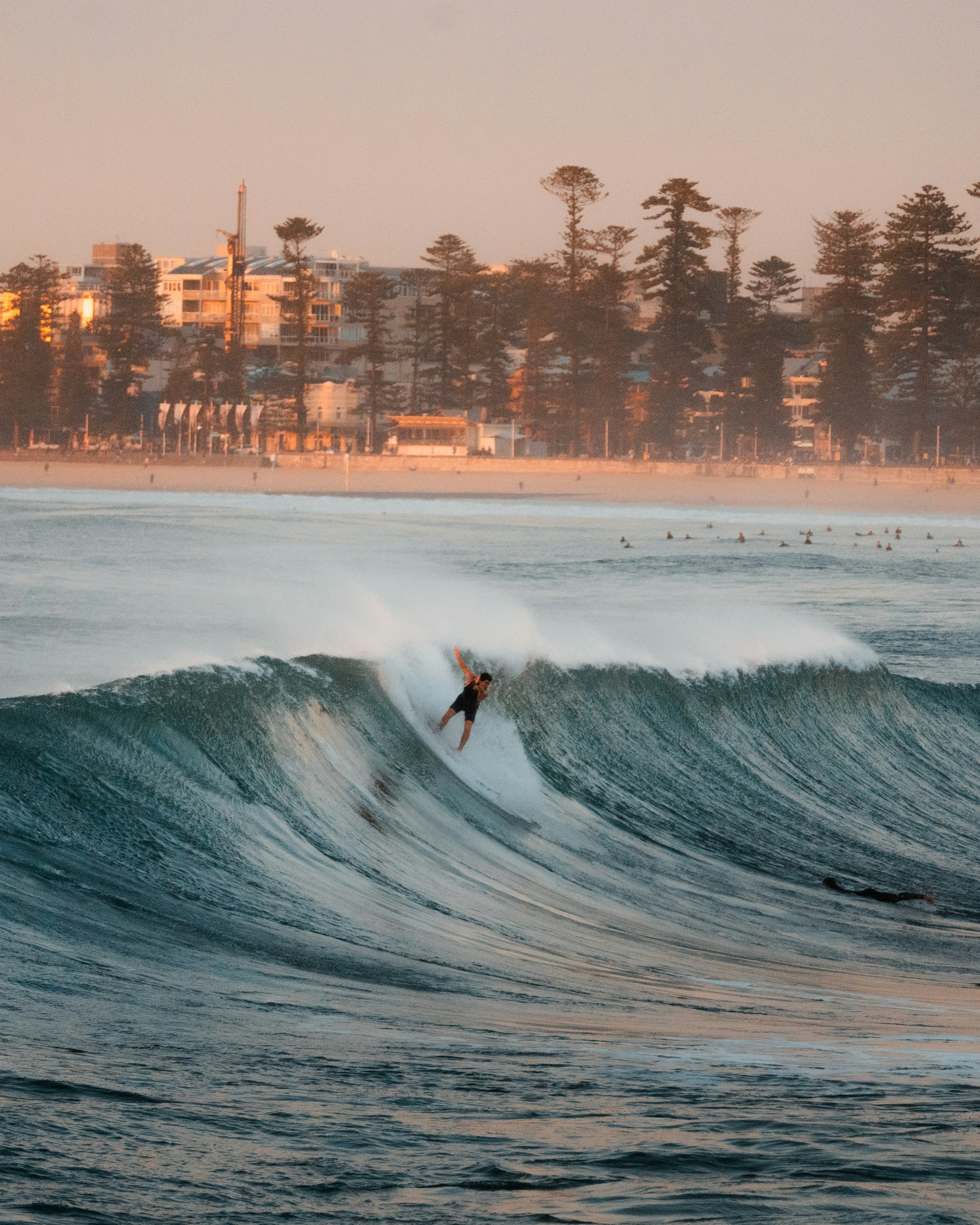 Surfer riding a large wave near a coastal town.