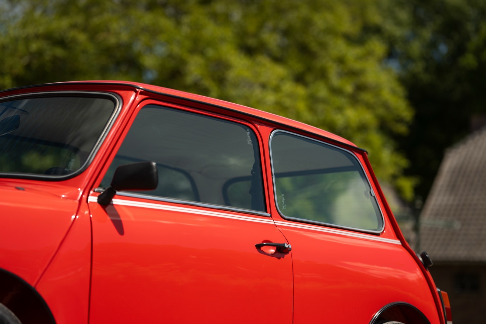 A close-up of a red car door with trees blurred in the background, showcasing its classic design.