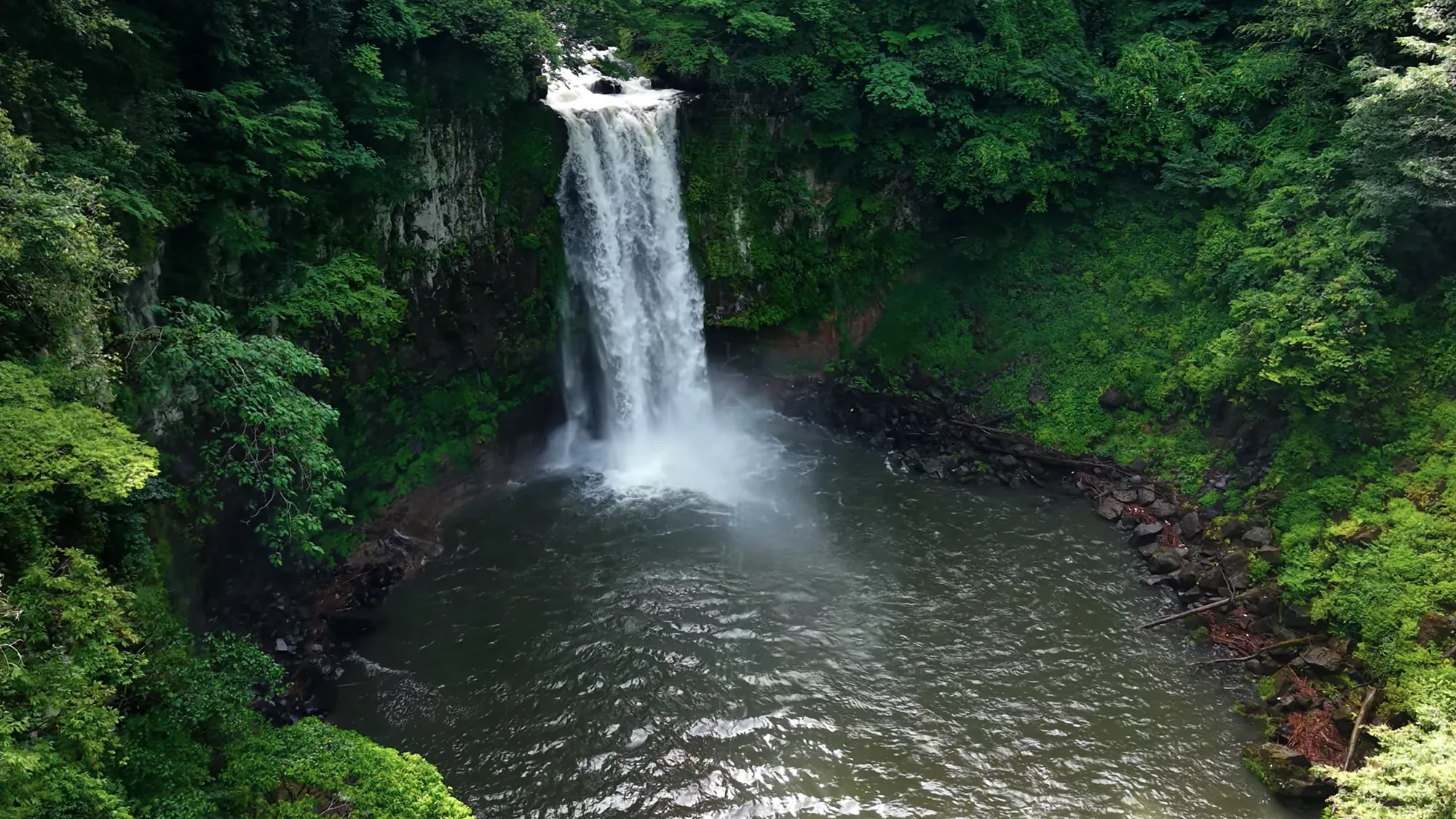 Aerial view of a waterfall falling into a green plunge pool near Kurokawa Onsen