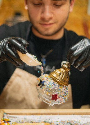 A person carefully applying colorful mosaic pieces onto a lamp in a workshop setting, demonstrating the artistic process in an Istanbul mosaic crafting workshop.