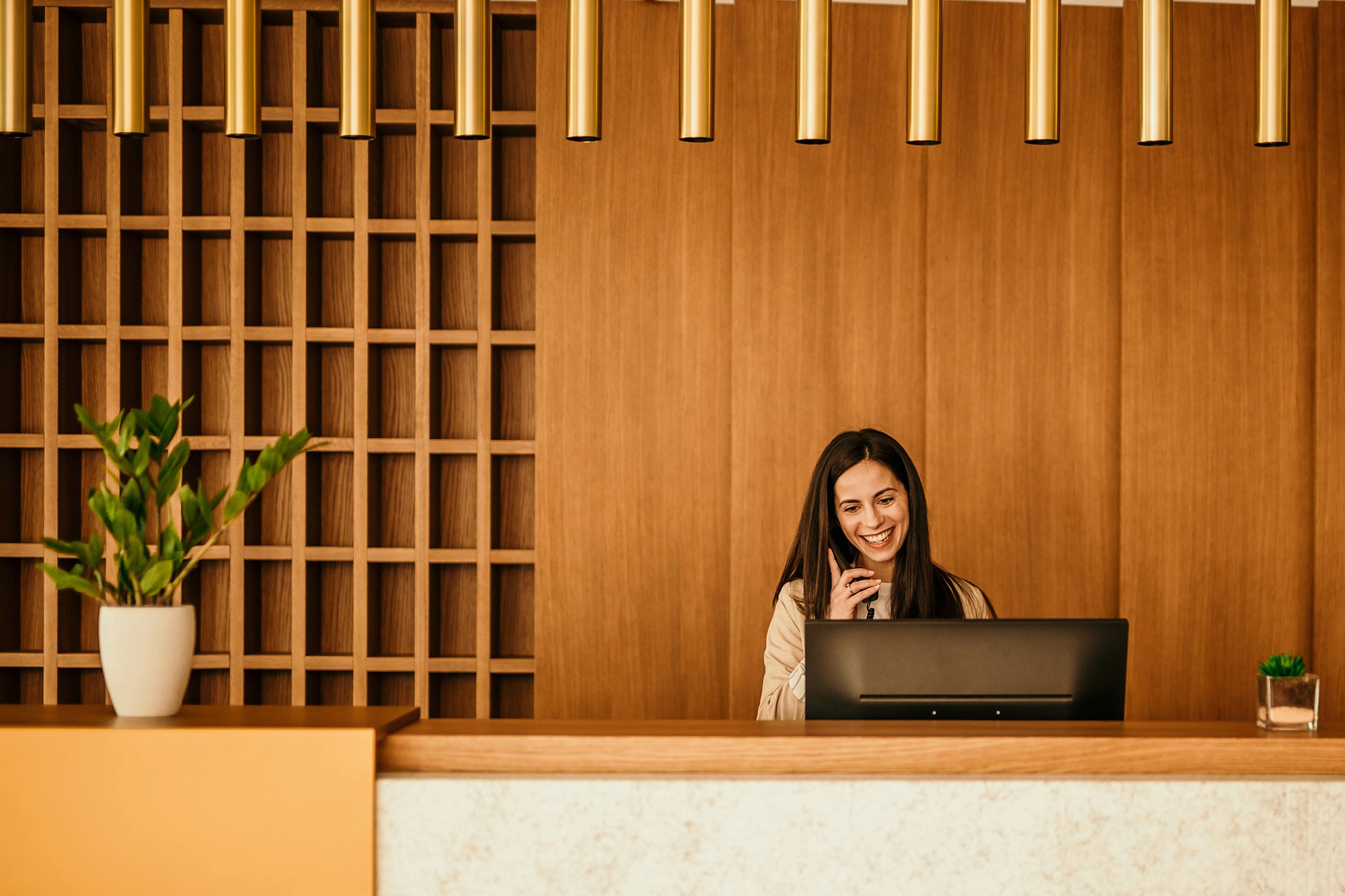 A hotel receptionist talks on the phone at a warm, wood-paneled front desk, creating a cozy, inviting atmosphere.