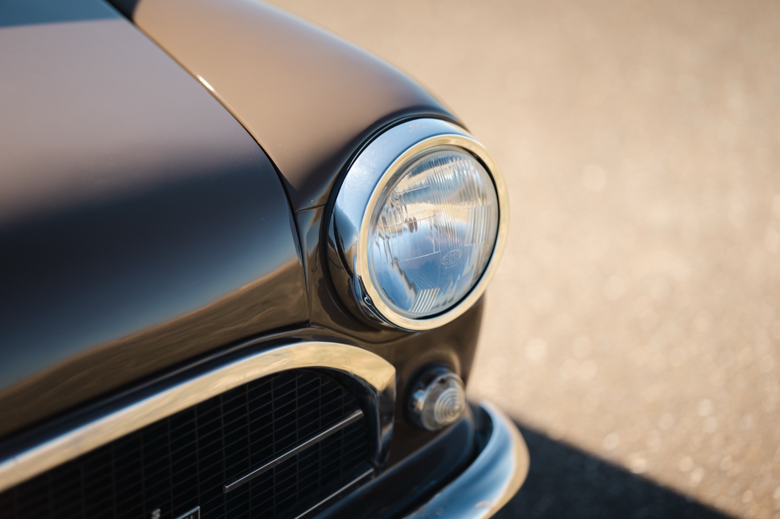 Close-up of a vintage car hood ornament with a reflective surface, set against a blurred background.