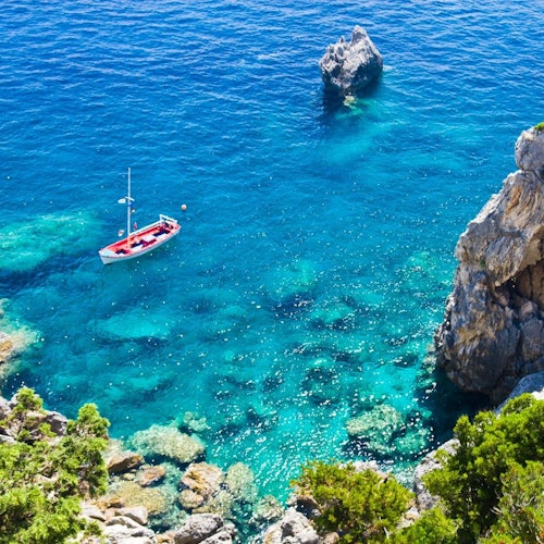 一艘紅色屋頂的小船漂浮在清澈的綠松石色水域，附近是岩石懸崖和綠色植被。