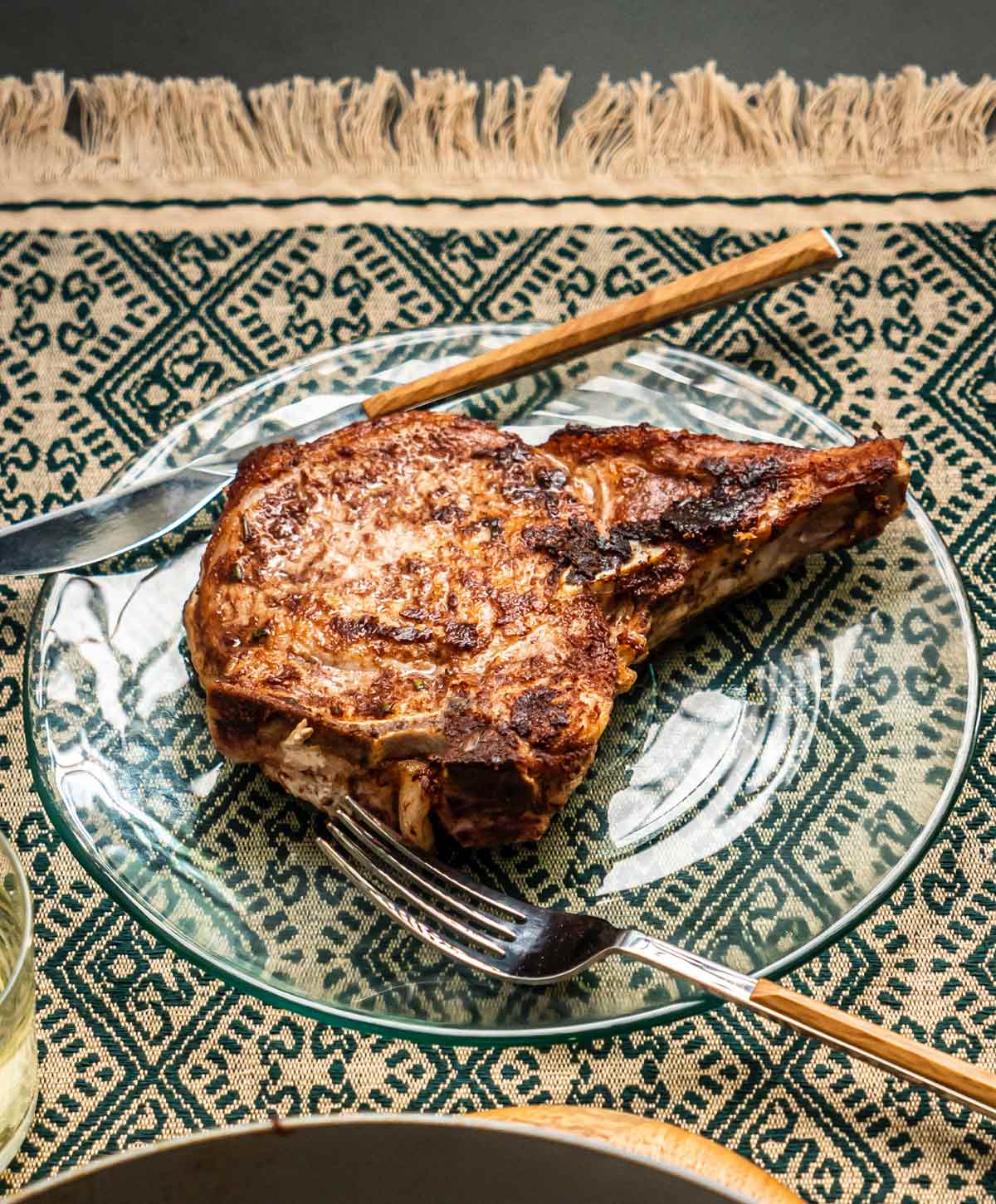 Cinnamon rosemary pork chop on clear glass and patterned table linens