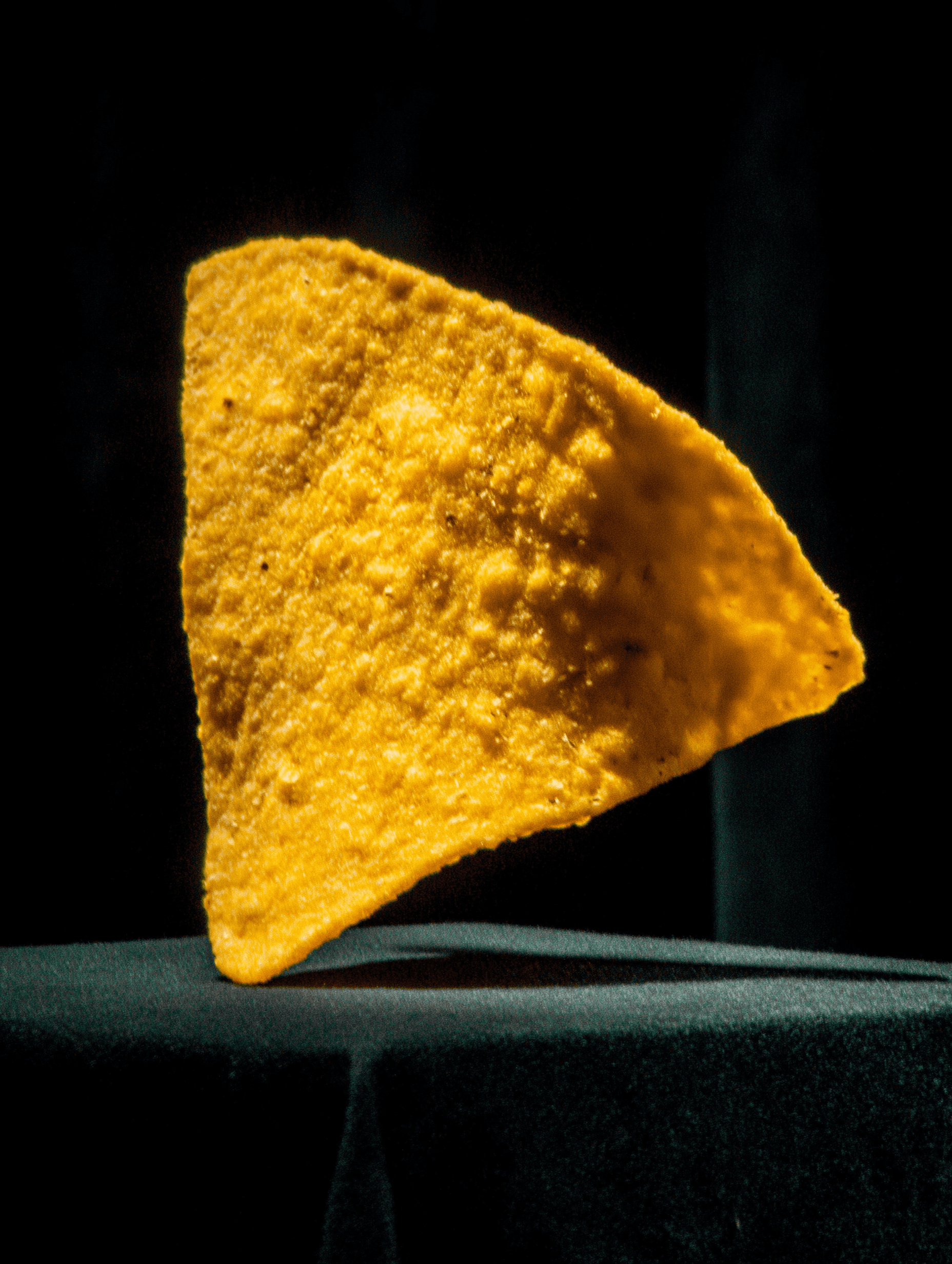 A single, golden-yellow tortilla chip with a textured surface, casting a shadow.