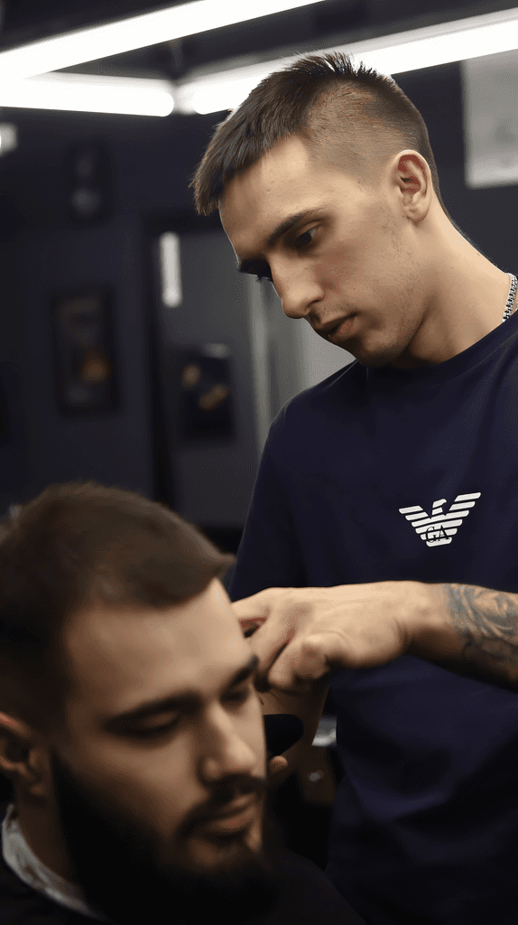 A barber styles a client's hair in a well-lit salon, focused on creating a precise look.
