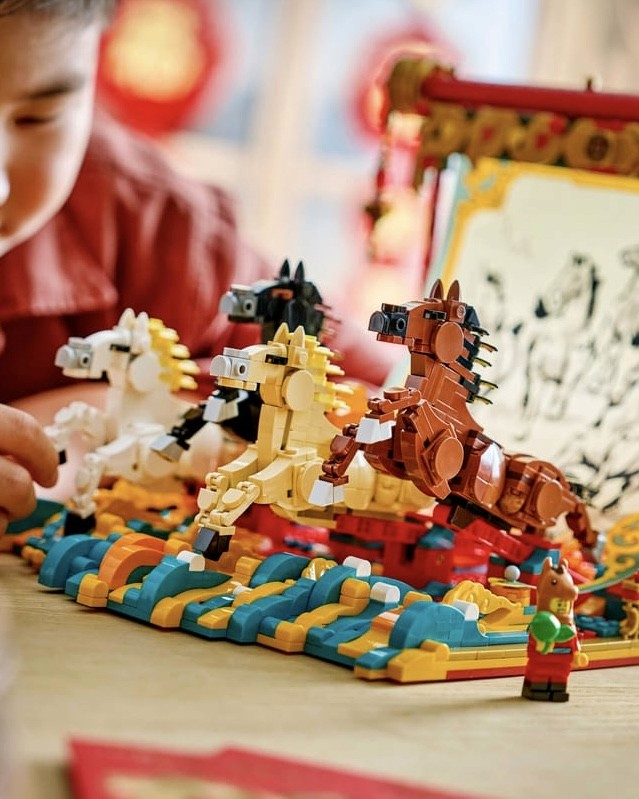 A child playing with a colorful Lego set featuring toy horses in various colors, set against a decorative backdrop.