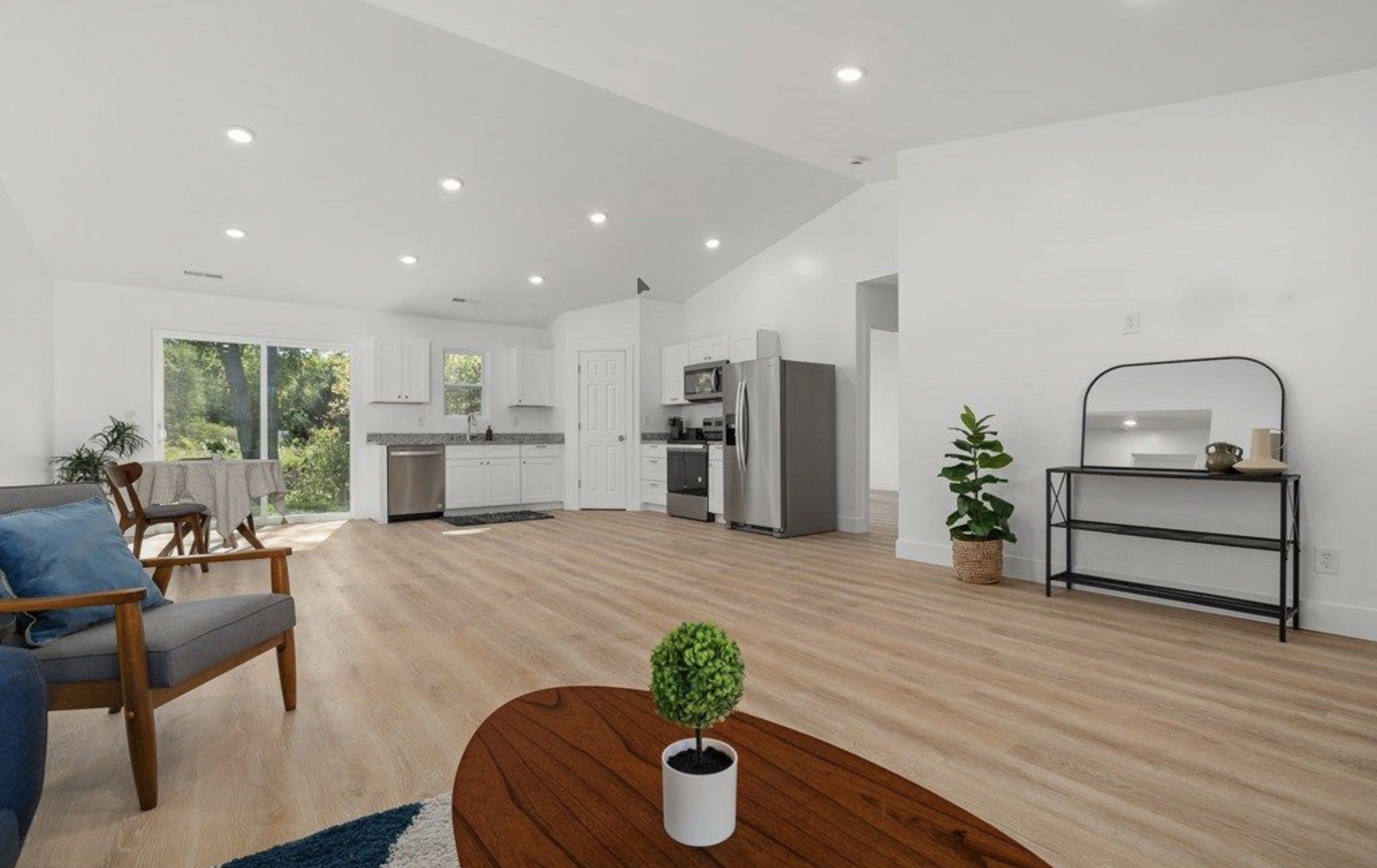 An open-plan living room and kitchen with vaulted ceiling, white cabinets, stainless appliances and light wood-look floors