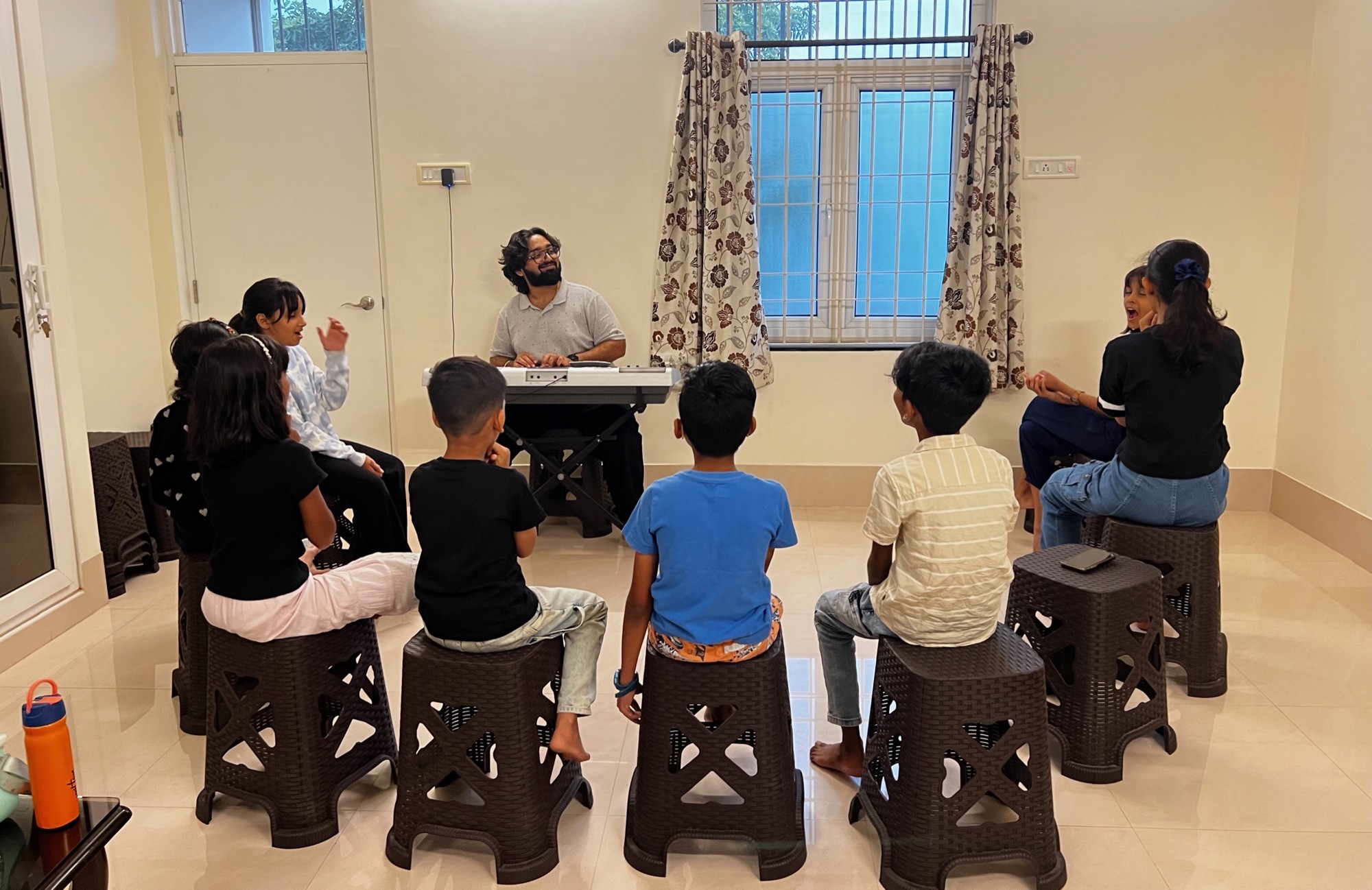 Vocal coach Sankalp at the keyboard with children seated in a circle on stools in Salem