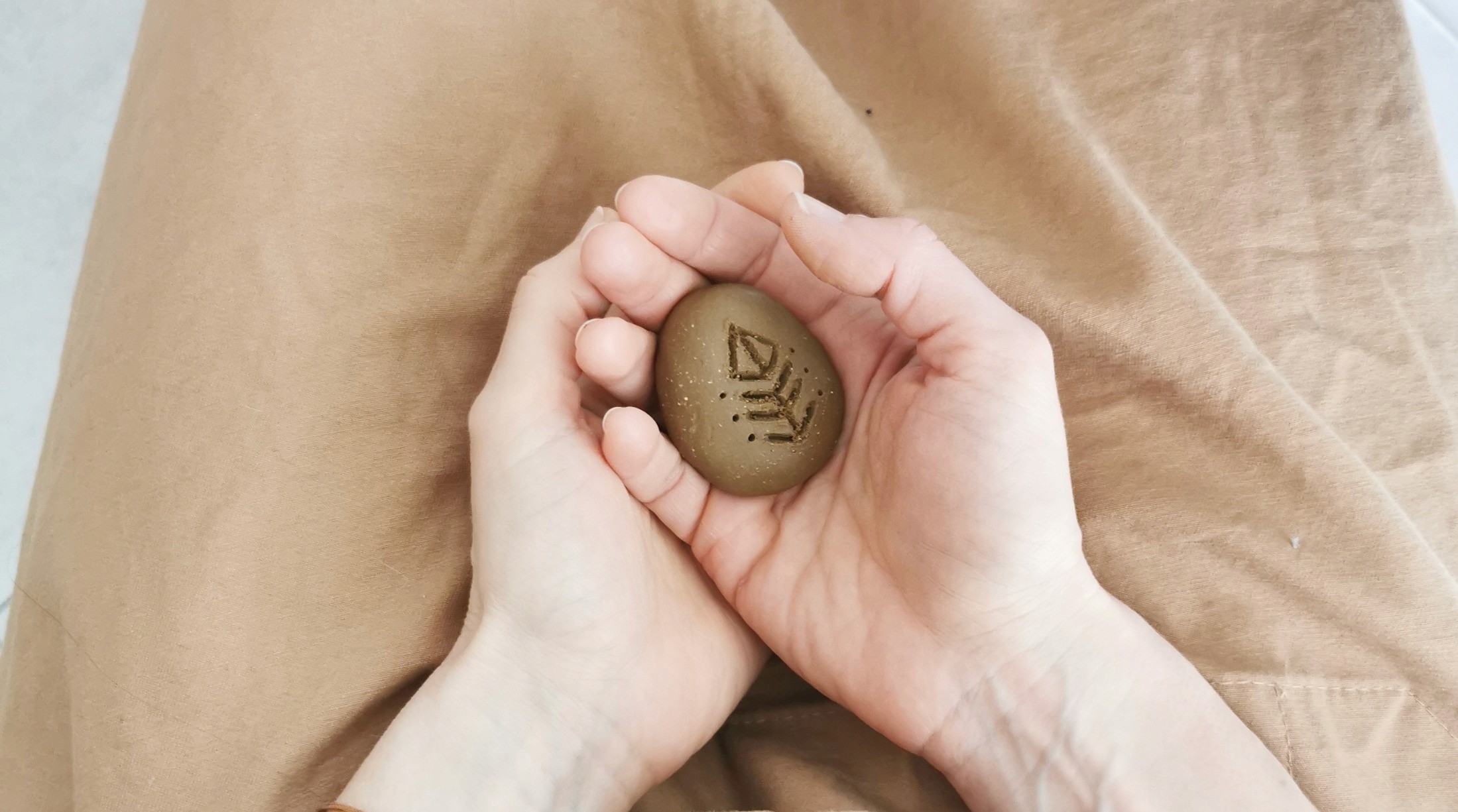 Cours céramique amulette : mains tenant une petite pièce en argile gravée de symboles, atelier Guérande