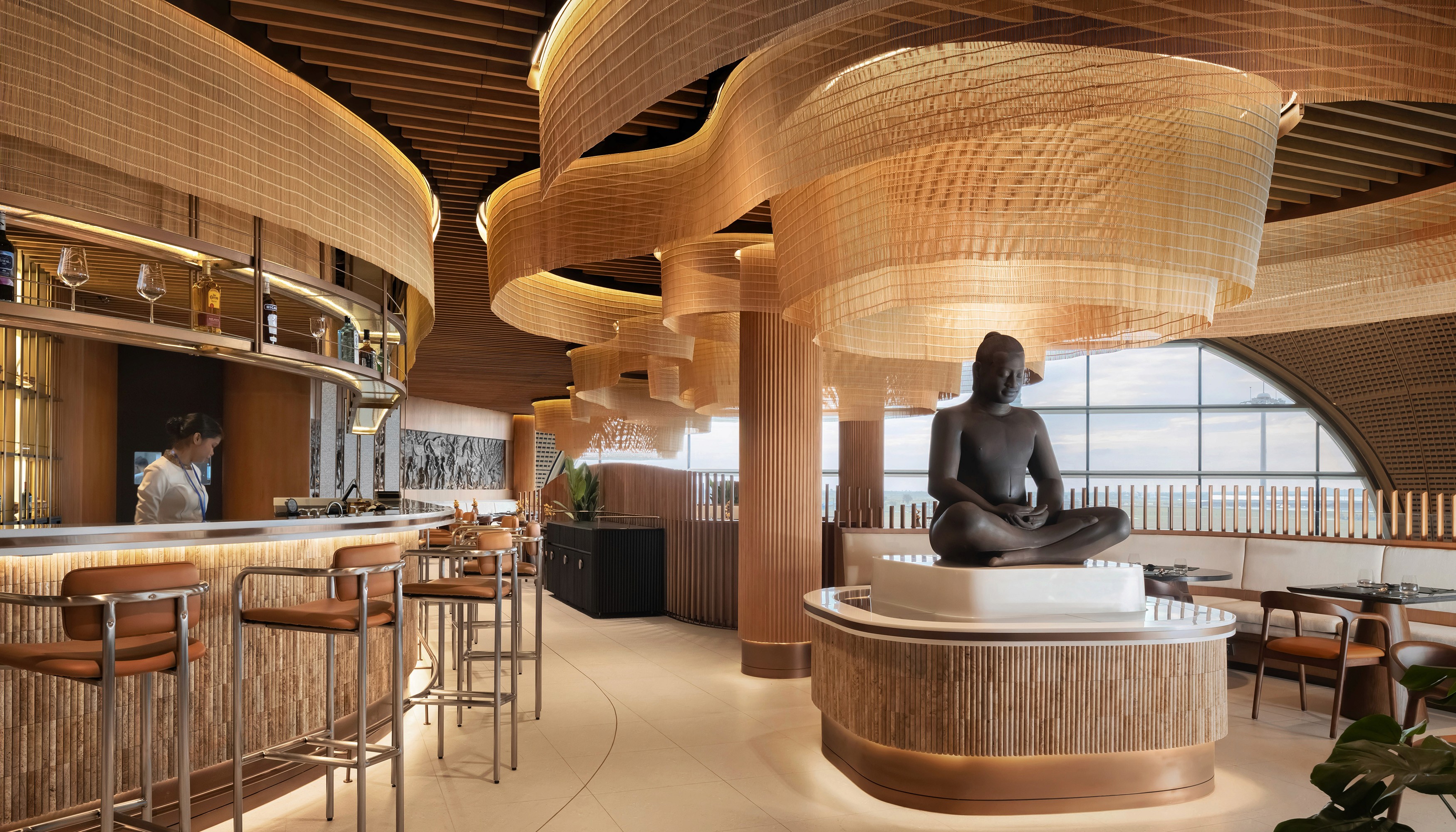 Interior detail of Malis Restaurant featuring a central Buddha statue and flowing mesh gold lighting fixtures balancing traditional Cambodian cultural elements with world-class contemporary design aesthetics
