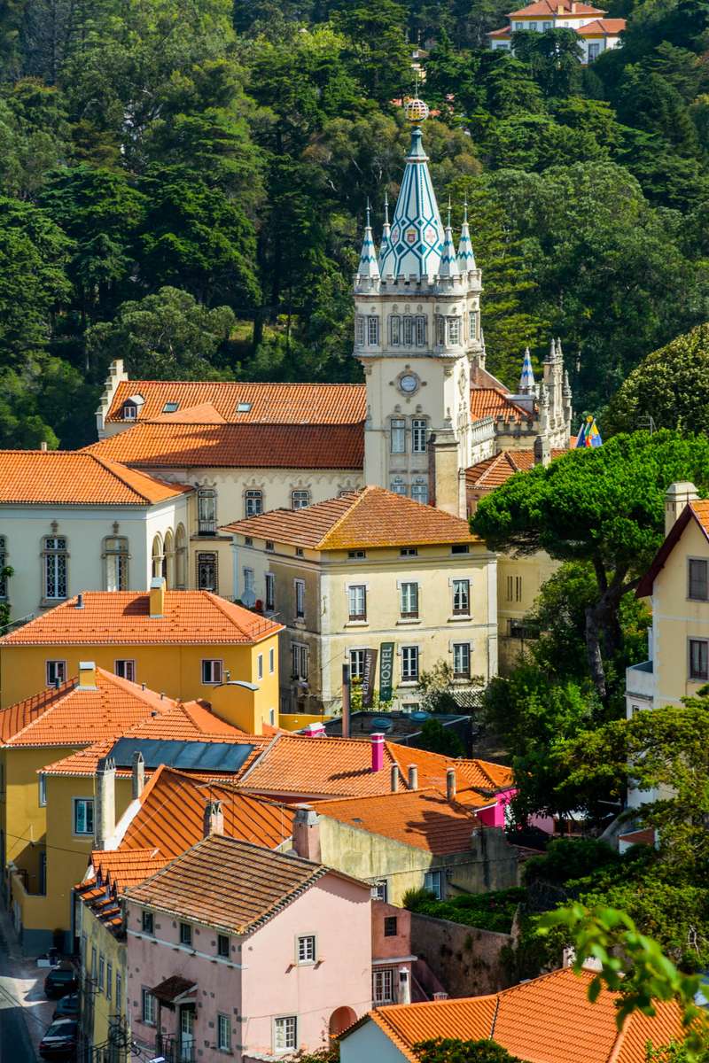 A high-angle view of a coastal town with terracotta roofs and a white church tower topped with a blue dome.