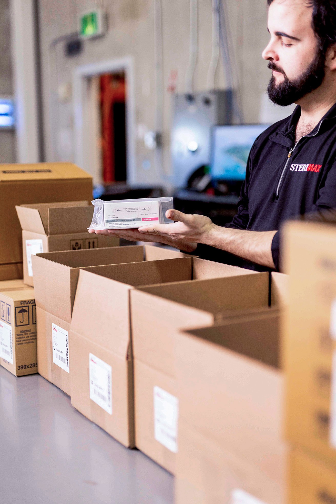 A SteriMax team member carefully inspecting a packaged pharmaceutical product in a distribution warehouse.