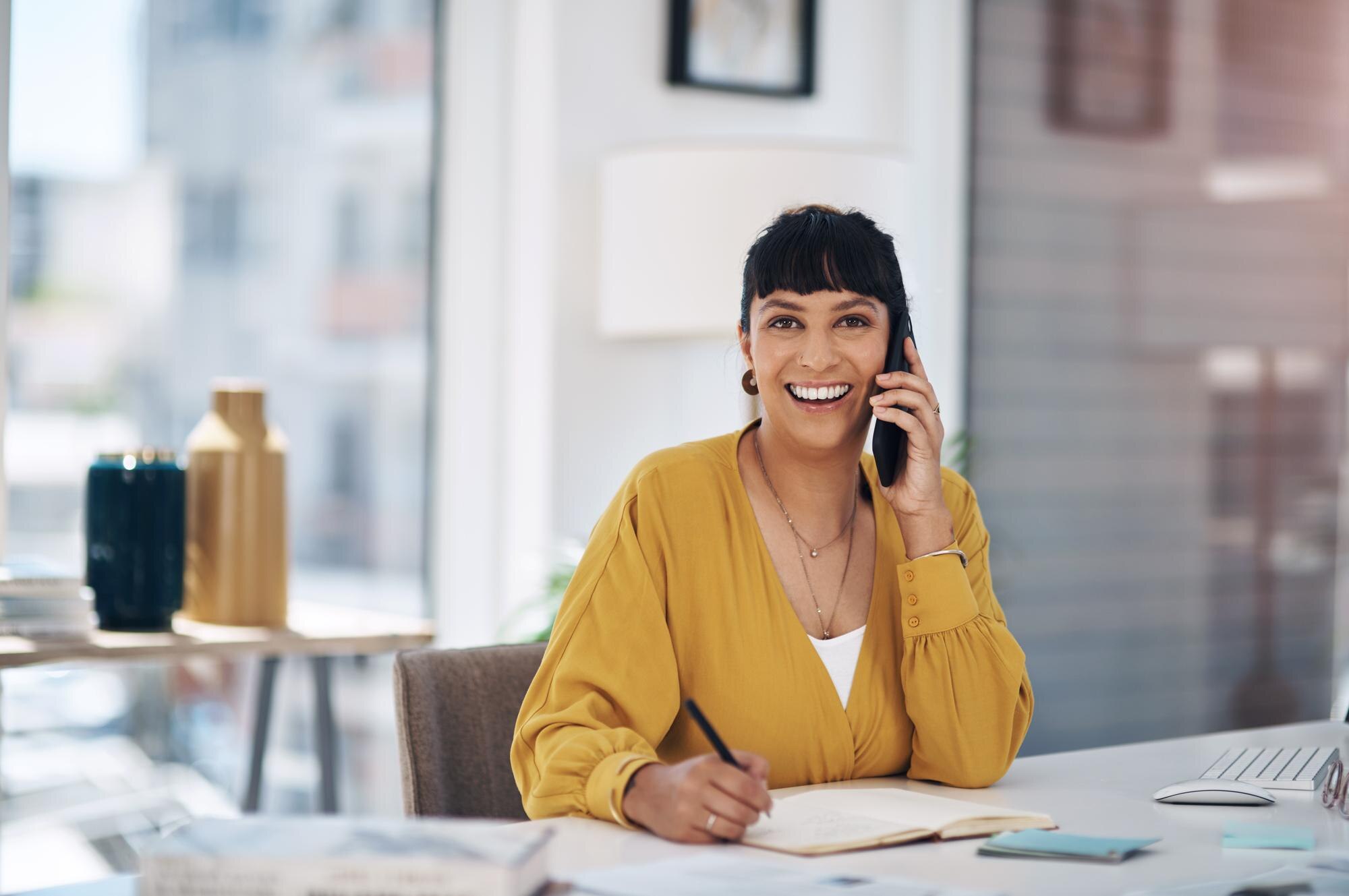 Professionele dienstverlener lacht terwijl ze telefoneert aan haar bureau