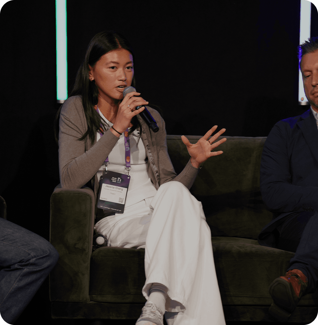 A panel discussion with three speakers, one woman gesturing as she speaks, seated on a couch.
