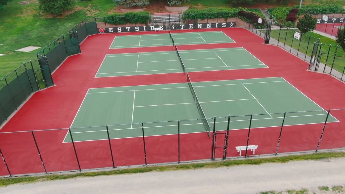 Aerial view of resurfaced Westside High School tennis courts with grass green playing areas, red out-of-bounds zones, and fresh white striping.