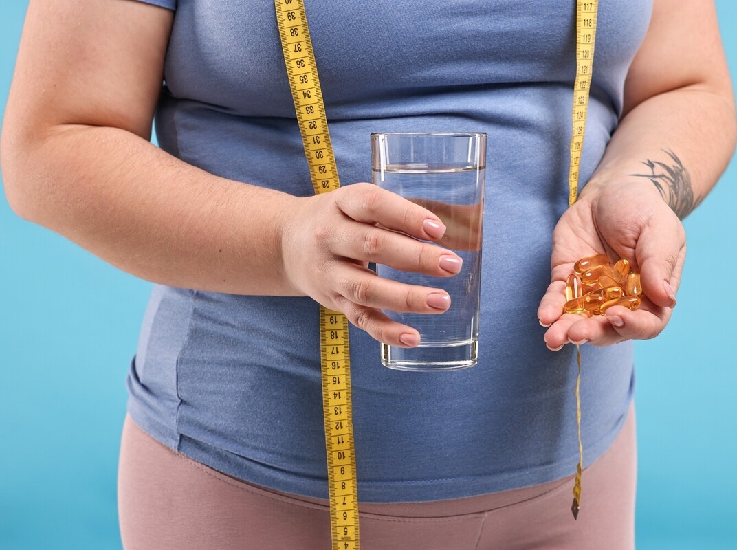plus-sized woman holding a glass of water and over-the-counter weight loss pills