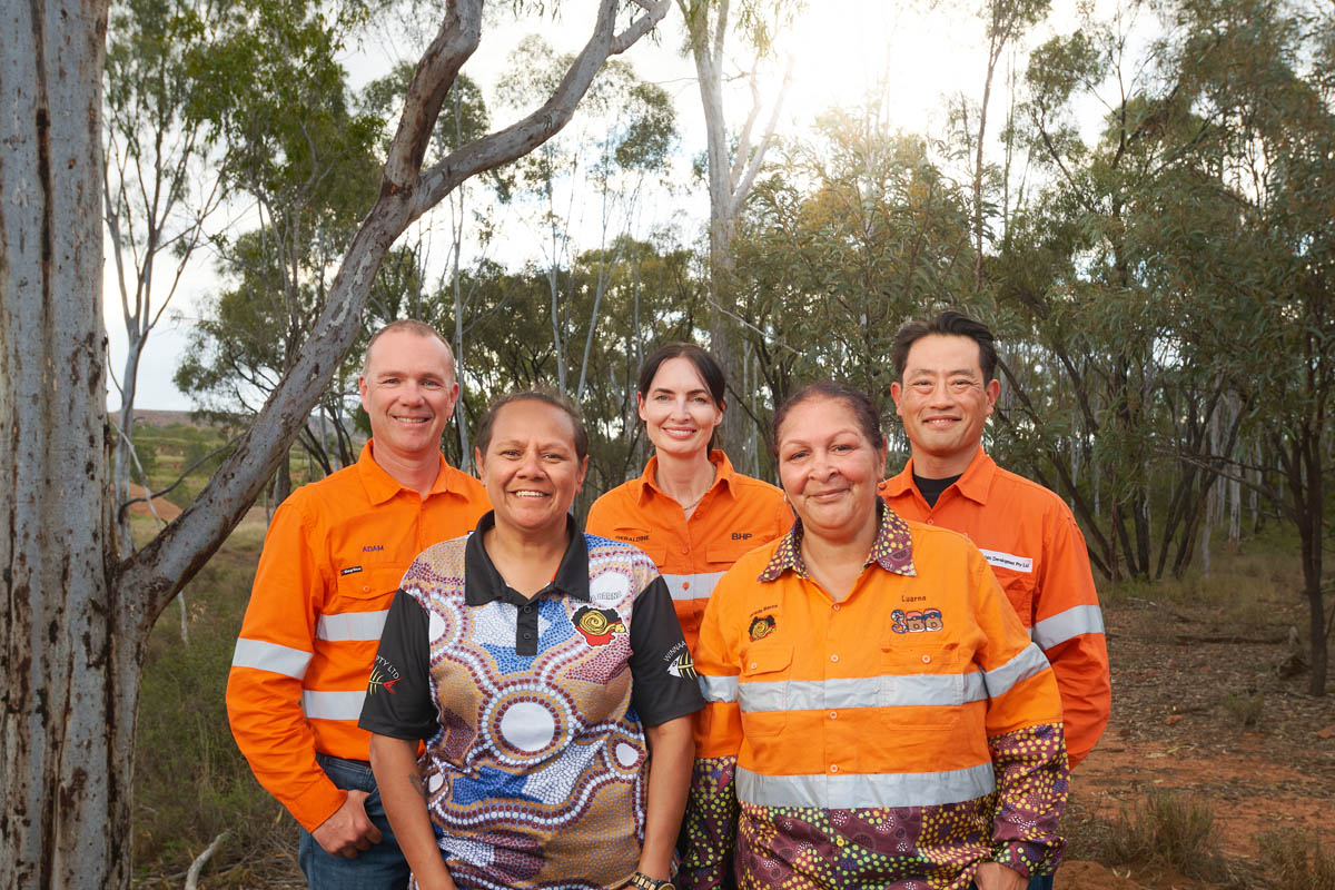 Diverse group of mine workers in hi-vis PPE outdoors, including Indigenous-designed shirt