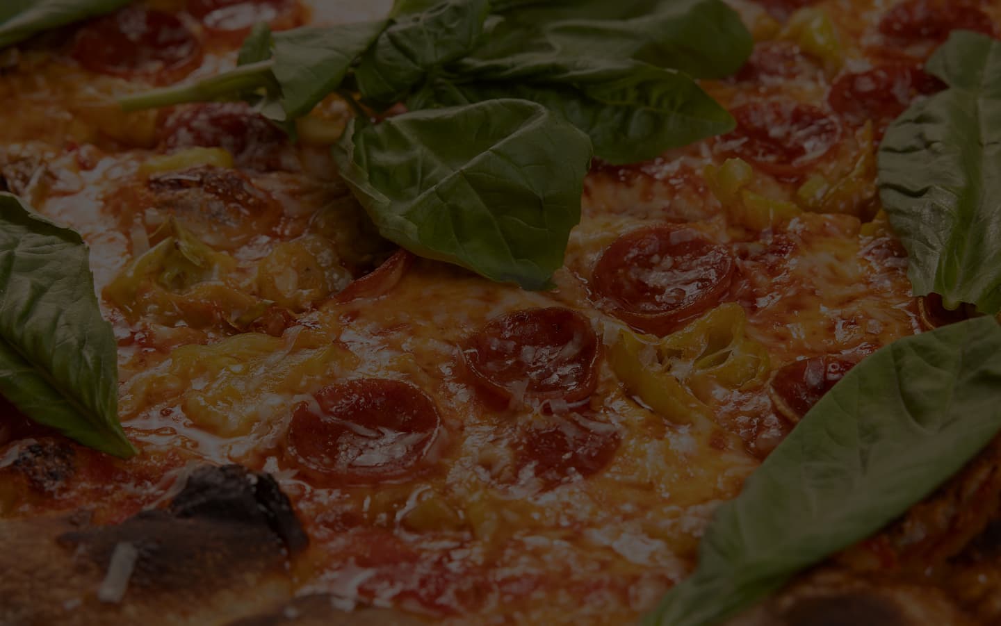 Close-up of a pepperoni pizza with melted cheese, basil leaves, and charred crust edges
