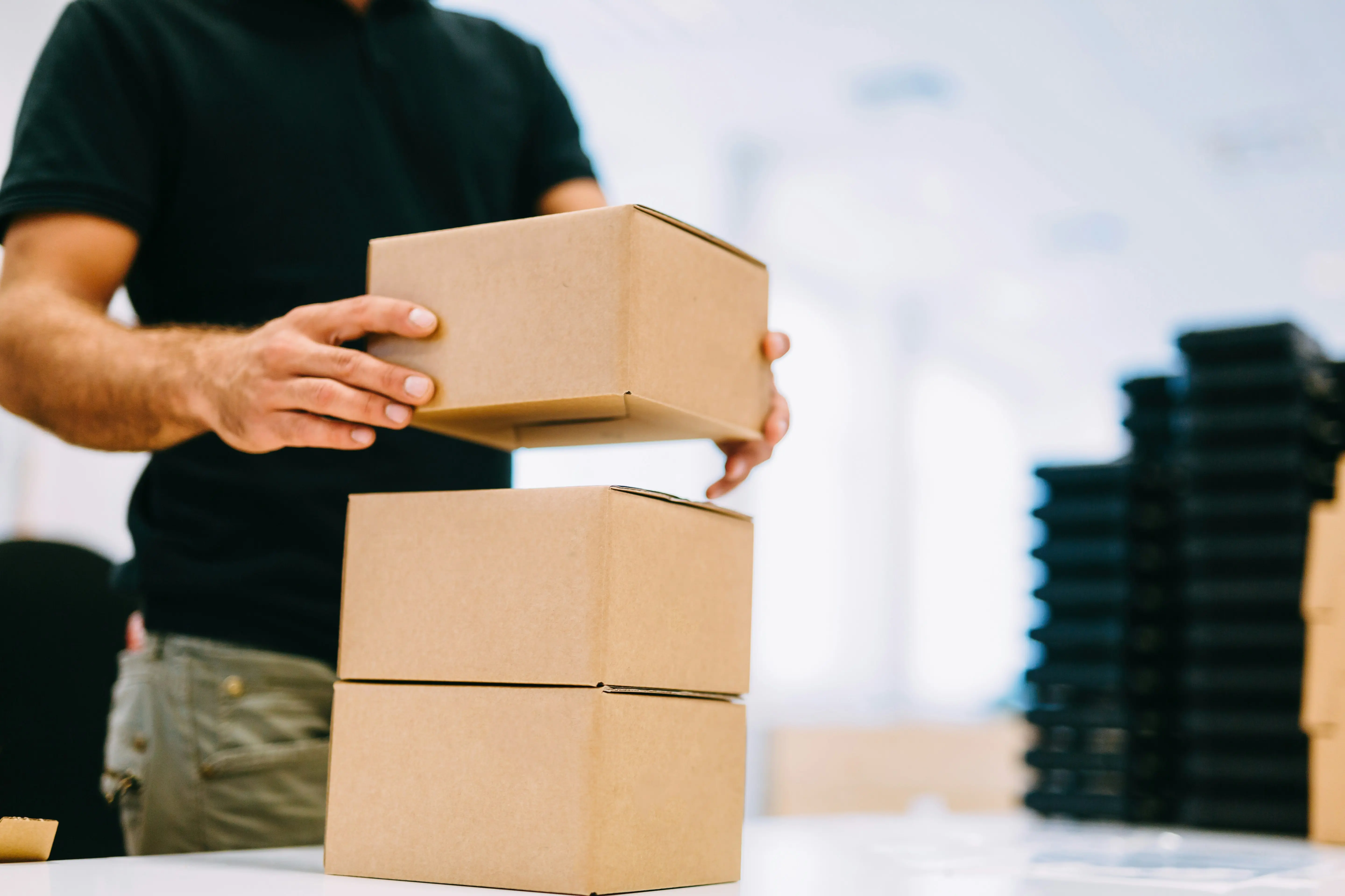 male warehouse worker places carboard boxes onto a packing table before dispatch
