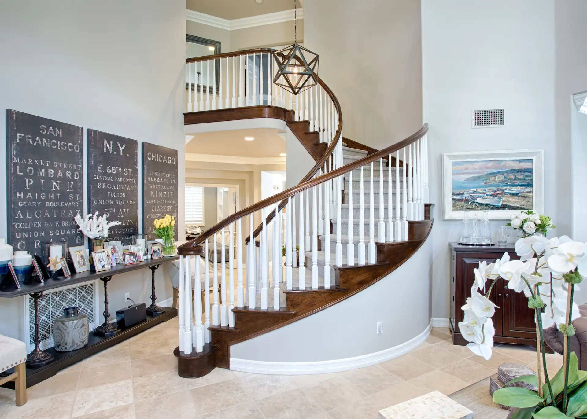 'Newport Beach Remodel' foyer with curved staircase, city-themed wall art, and a view into the living space.