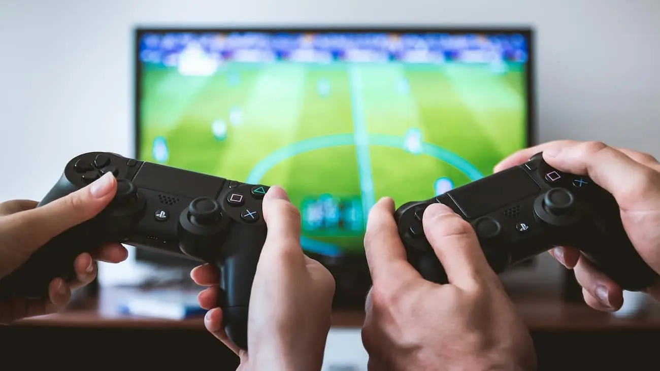 Zwei Personen spielen ein Fußball-Videospiel auf einer Spielekonsole, während sie die Controller in den Händen halten und das Fußballfeld auf dem Bildschirm angezeigt wird, optimiert für die Organisation von E-Sport-Turnieren mit CoachingArea.