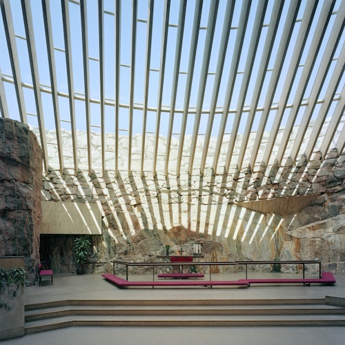 Avara sisustus, jossa on kalliot seinät ja viistoista palkeista koostuva kattoikkuna, sisältäen penkkejä ja kynttilöillä varustetun pöydän monitasoisella alustalla.