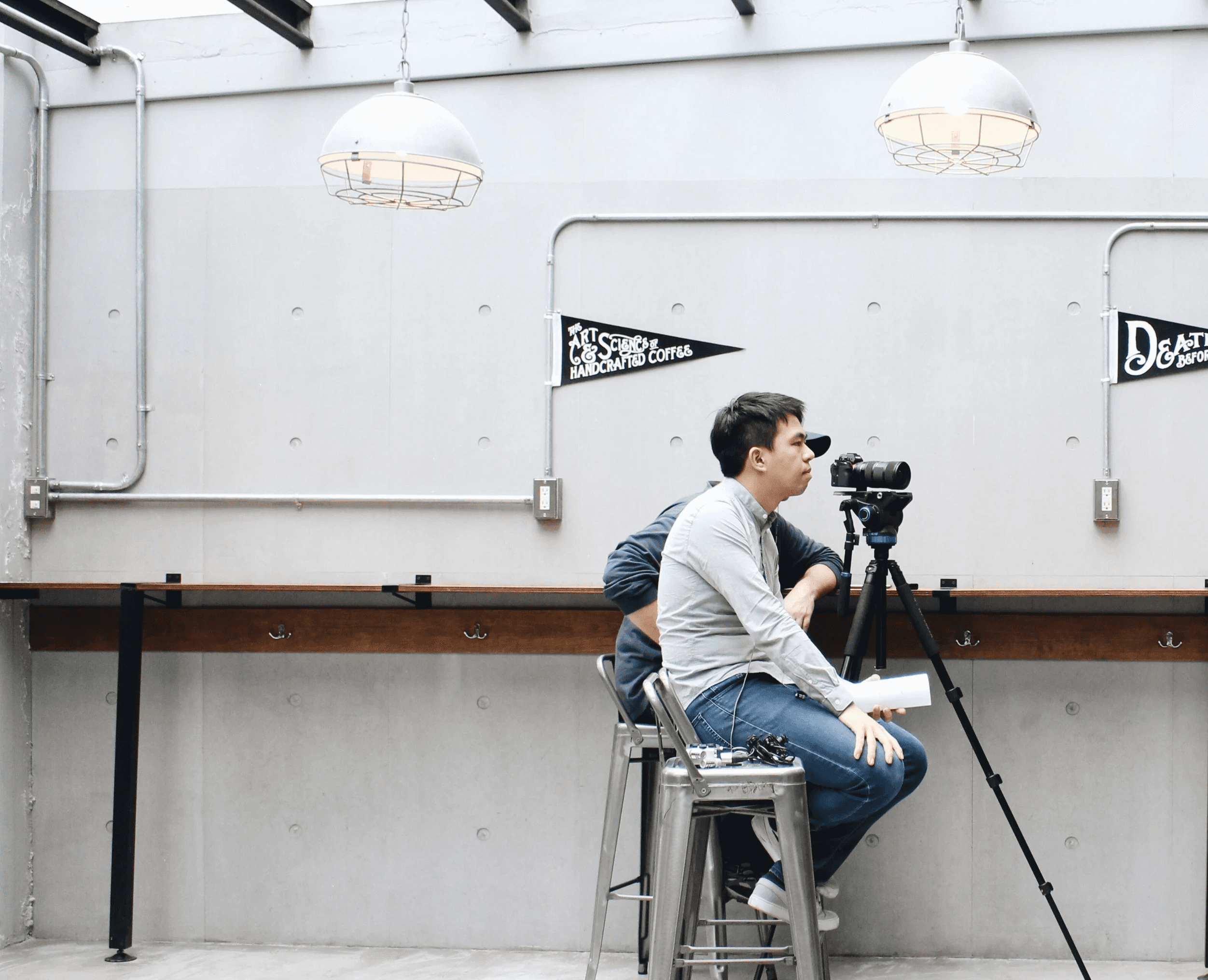 Jacob Chen sitting on a chair, in a coffee shop with industrial style interior, interviewing a person out of the shot, with cameras in the background.