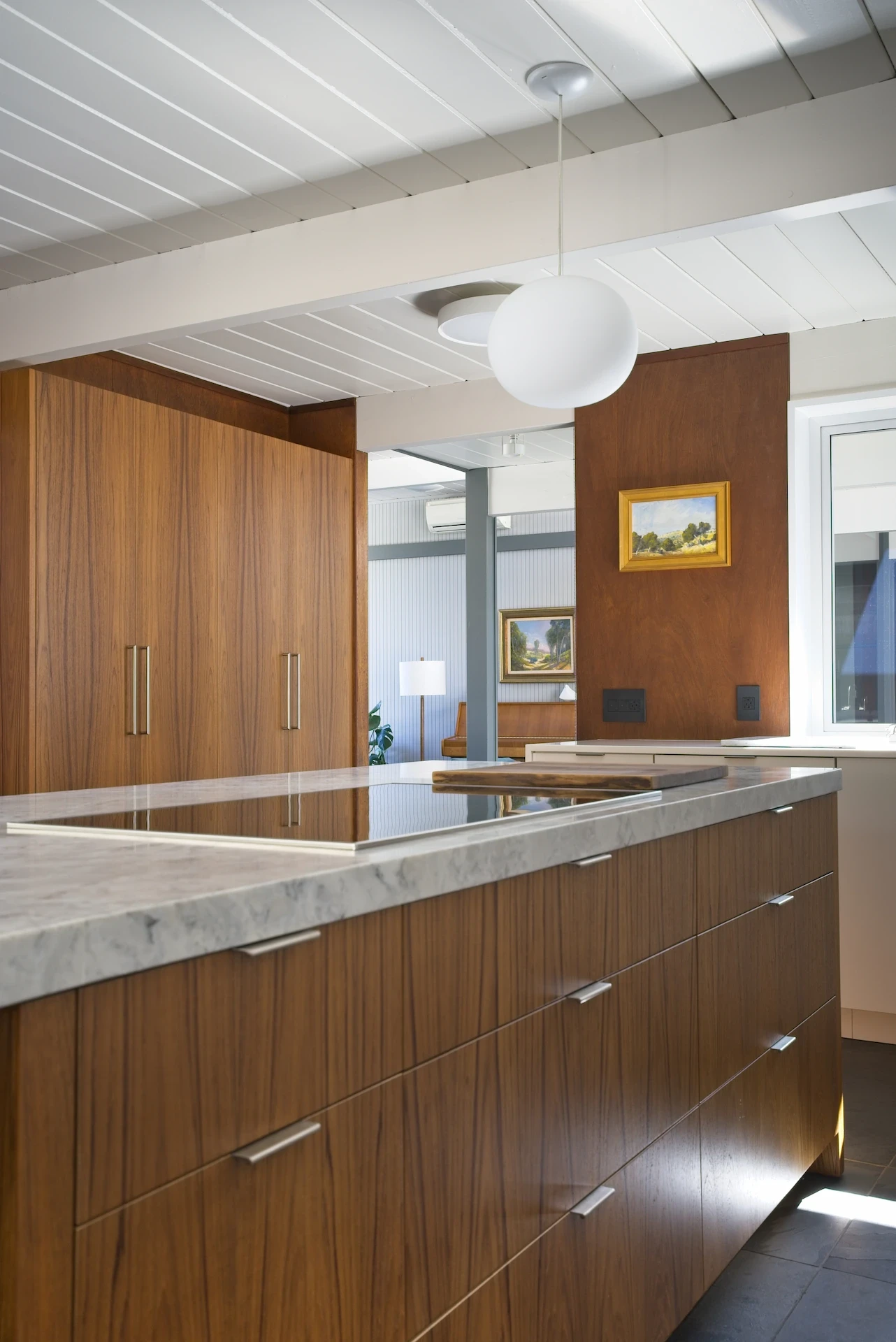 Angled portrait of the large kitchen island, featuring a leatherized quartzite countertop over custom walnut cabinetry, in the Eichler kitchen remodel. Photo by Todd Huge.