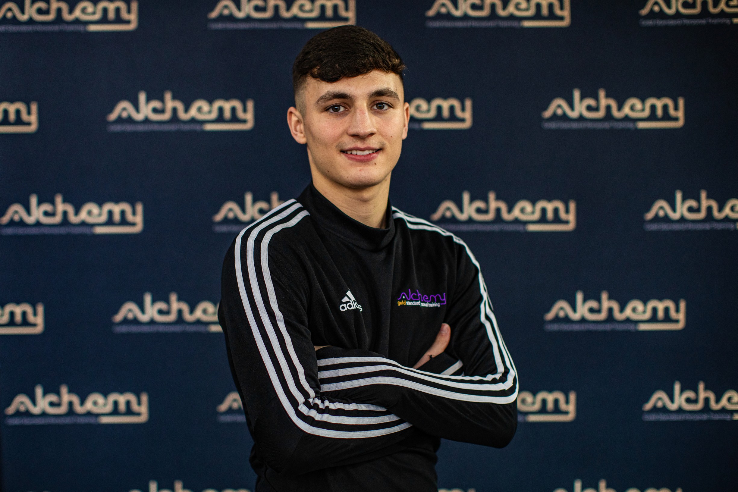 A personal coach is smiling with his arms crossed, wearing a black