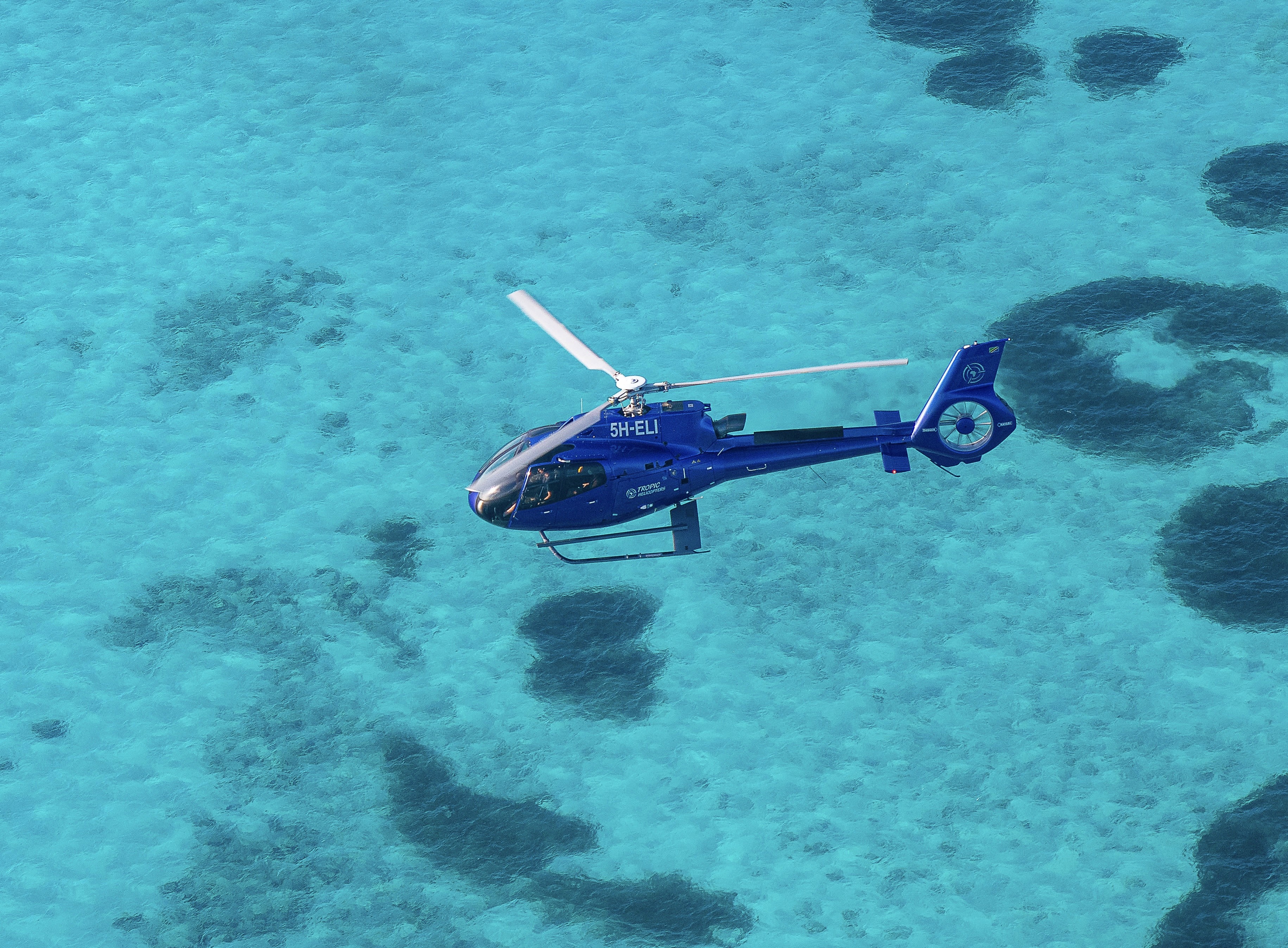 Helicopter flying low over the turquoise waters and coral reefs off the coast of Zanzibar
