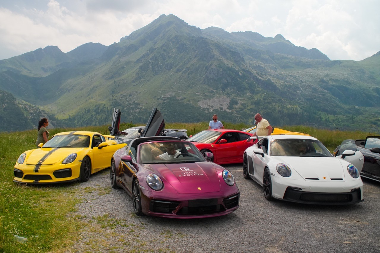 Porsche 911 et voitures de sport garées dans une prairie au pied des montagnes, road trip Italie