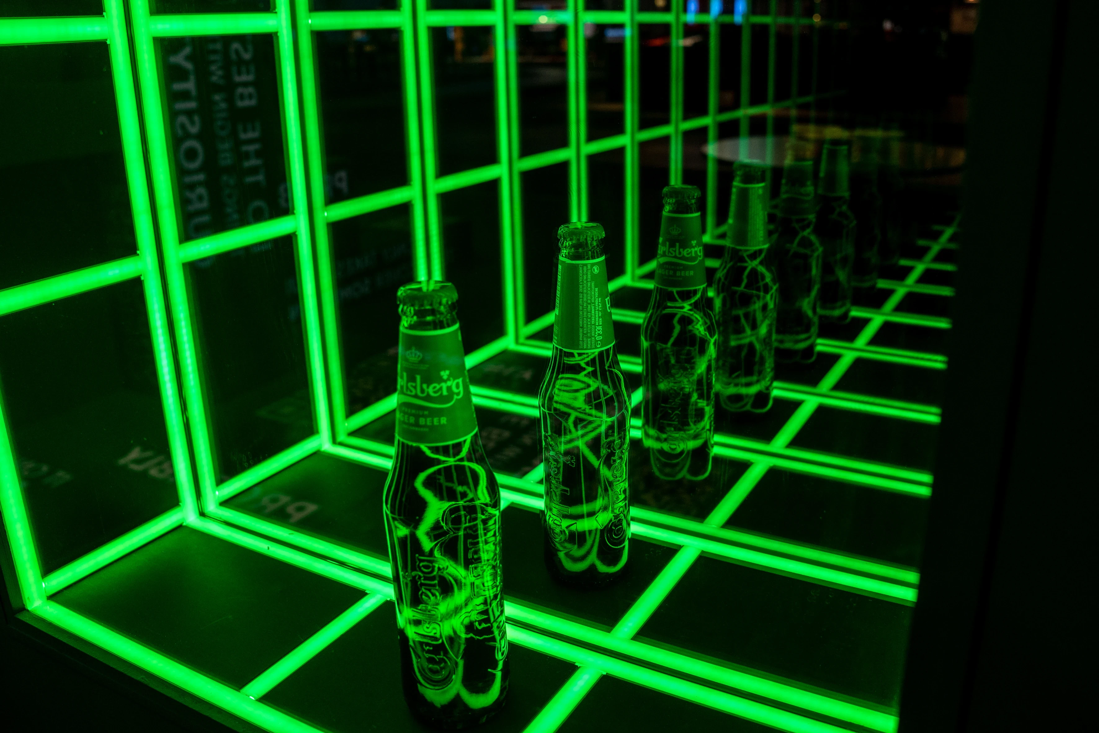 Engraved Carlsberg bottles glowing green in an infinity mirror installation of neon grid lines.