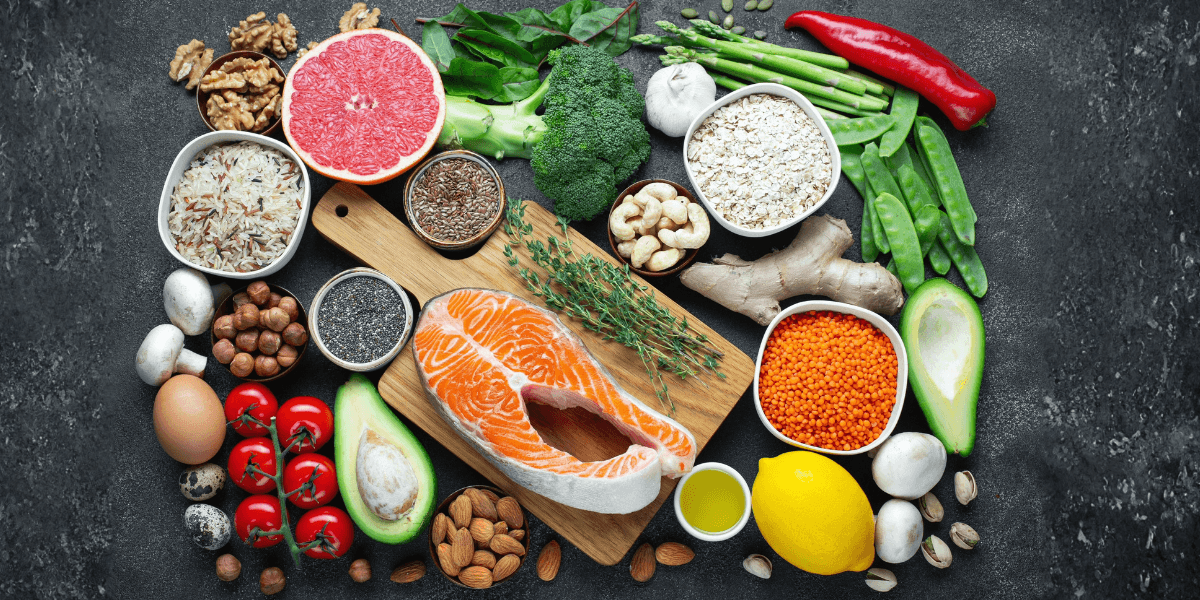 Colorful array of healthy foods, including salmon, avocado, vegetables, nuts, and grains, emphasizing protein-rich options for wellness