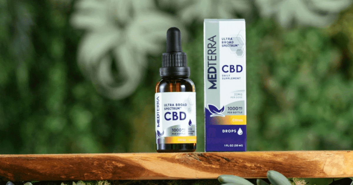 A bottle of Medterra CBD oil placed on a wooden surface next to its product packaging, with green plants in the background.
