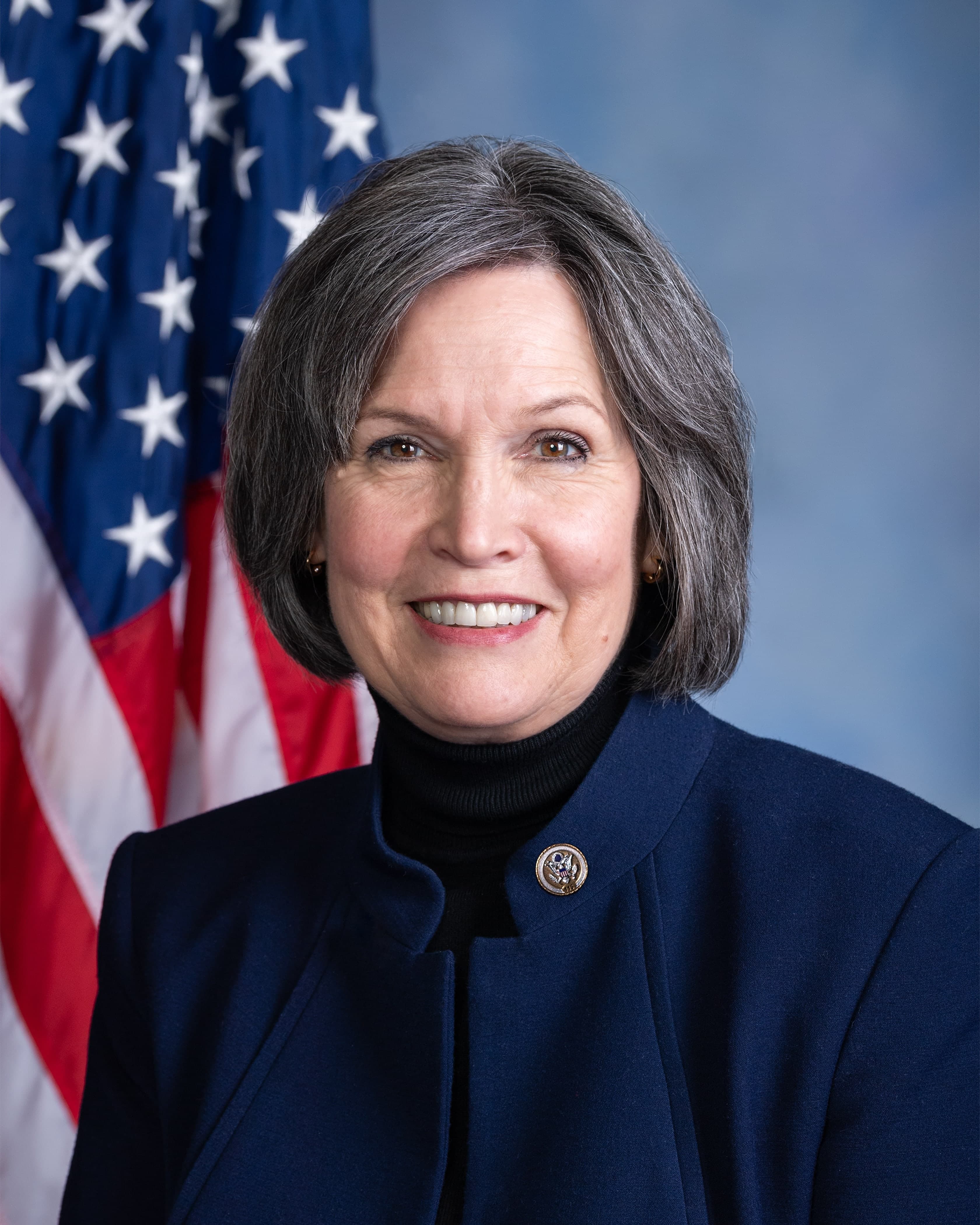 Portrait of Betty McCollum on a blue background with a portion of the flag of the United States of America in view behind subject