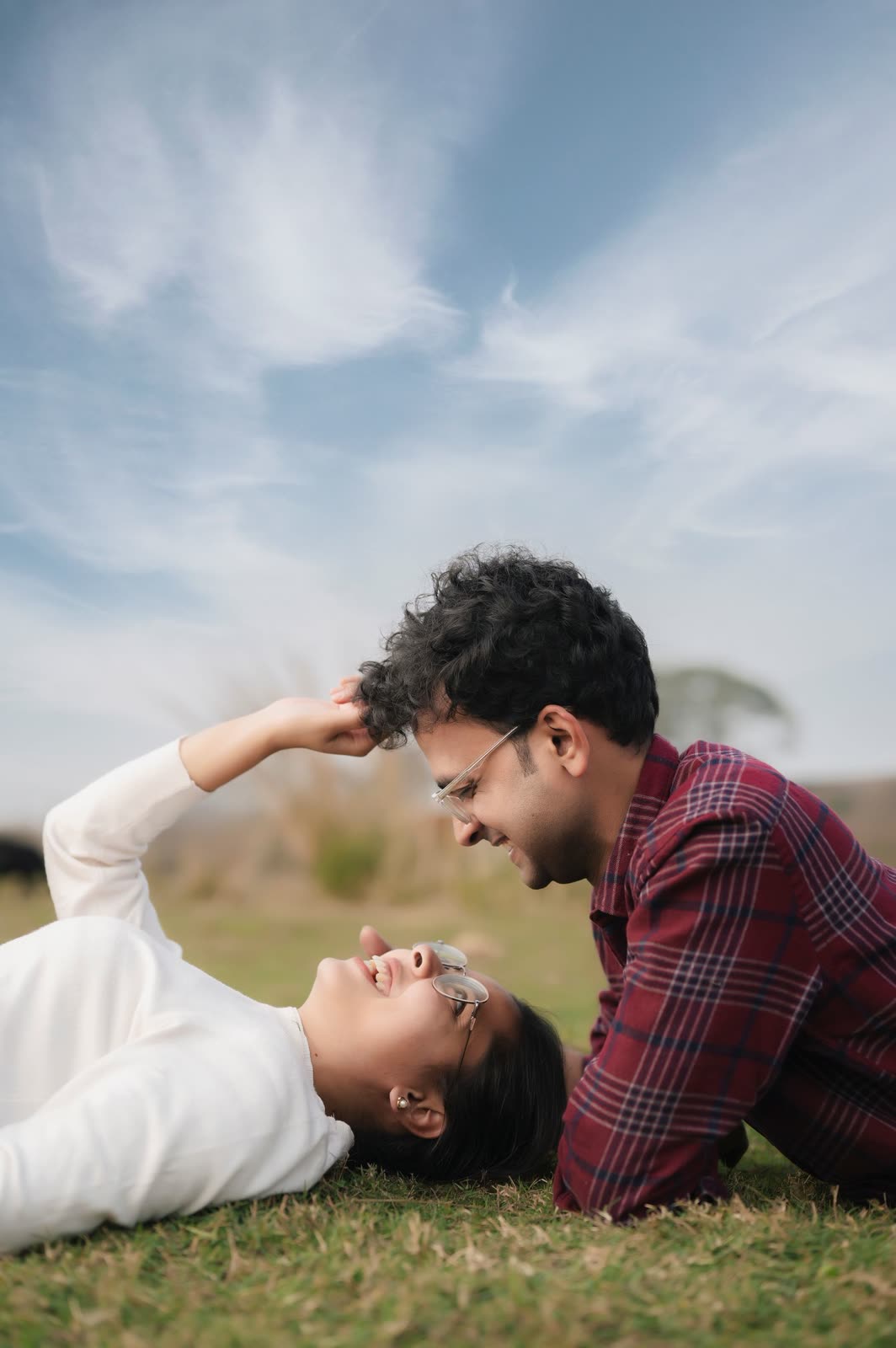 Couple lying on grass with the woman reaching up toward the man's hair