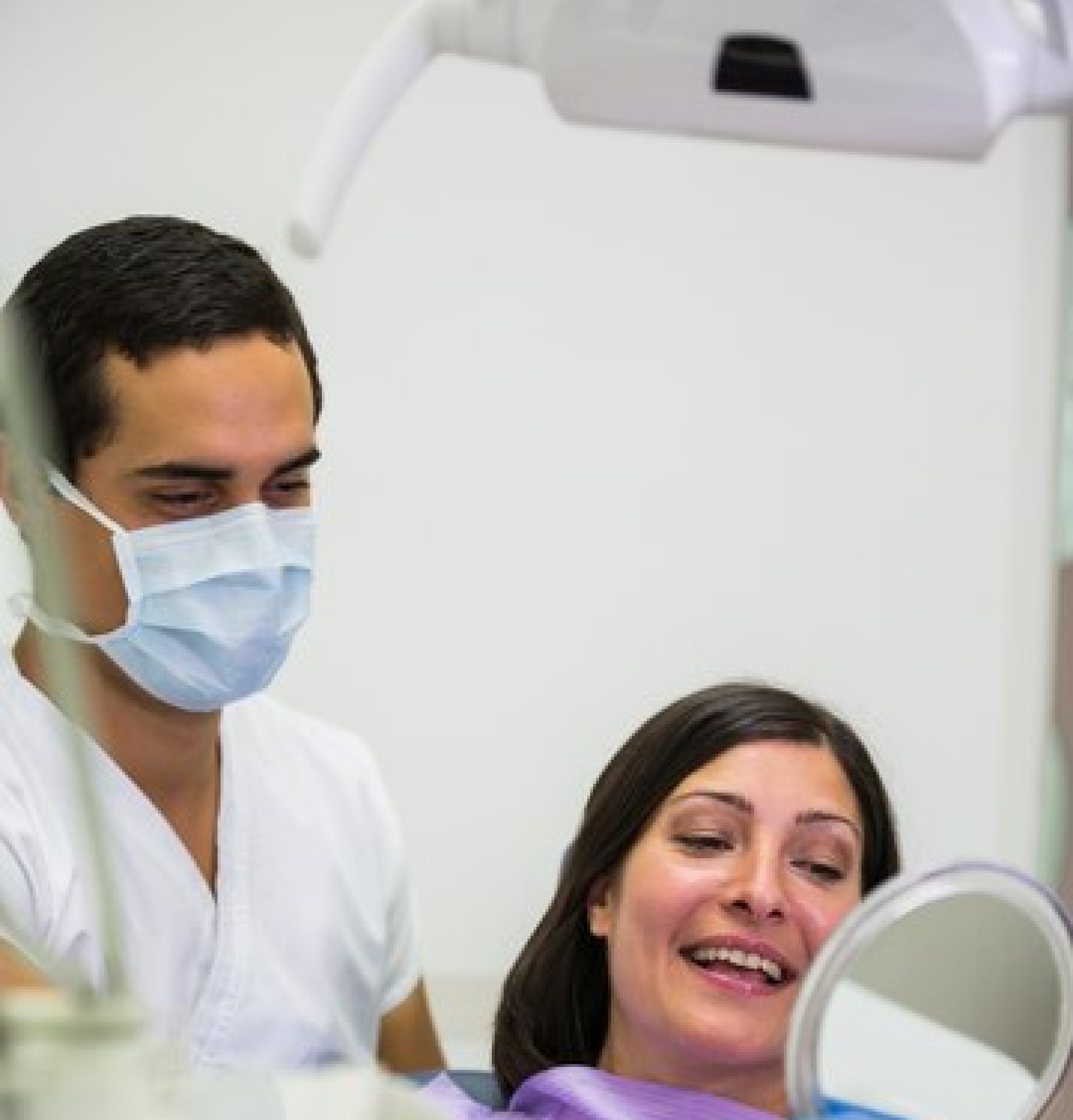 A dentist wearing a mask showing a female patient her dental X-ray, both smiling and discussing the results