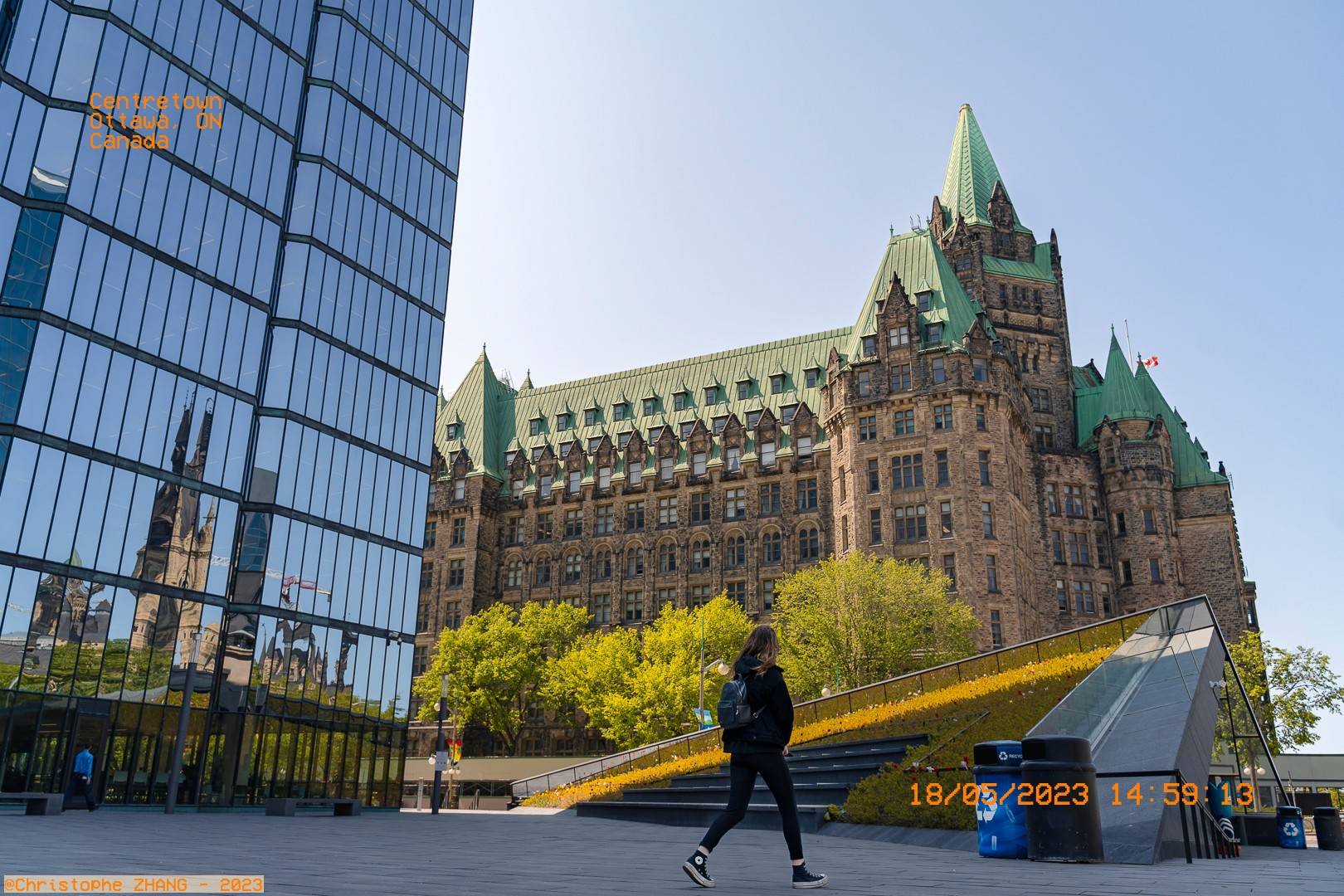 Personne marchant devant le château Laurier, reflété dans un bâtiment en verre à Ottawa.