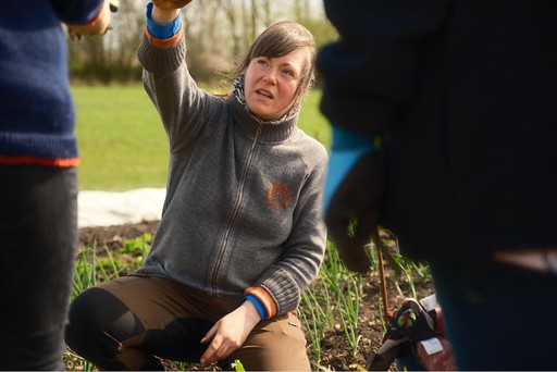 Anne sidder på hug foran deltagerne på Årshaveforløbet hos Egebjerggård Grønt. 