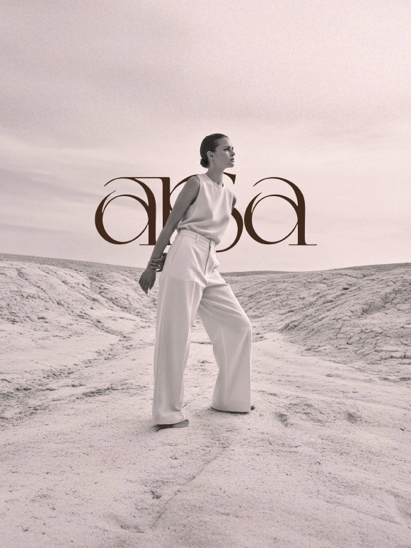 A model stands confidently in a barren landscape, wearing a sleeveless top and high-waisted, wide-legged trousers. The image is monochromatic with soft tones, emphasizing the textured ground and subtle contours of the terrain. The brand name arsa is prominently integrated into the design, adding a modern touch to the scene.