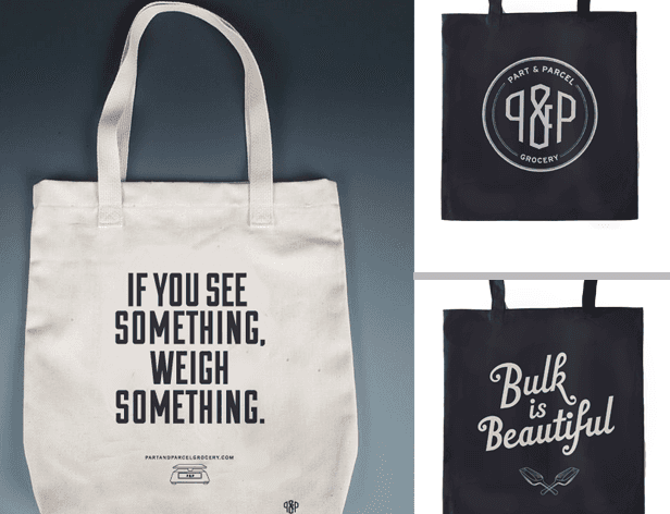 The image shows two tote bags displayed side by side against a dark gray background. The bag on the left is white and features the text "IF YOU SEE SOMETHING, WEIGH SOMETHING." printed in black. Below the text, a small graphic of a cash register is visible. The bag on the right is black and displays the text "Bulk is Beautiful" in white letters. A small logo is visible near the bottom right corner of the black bag.