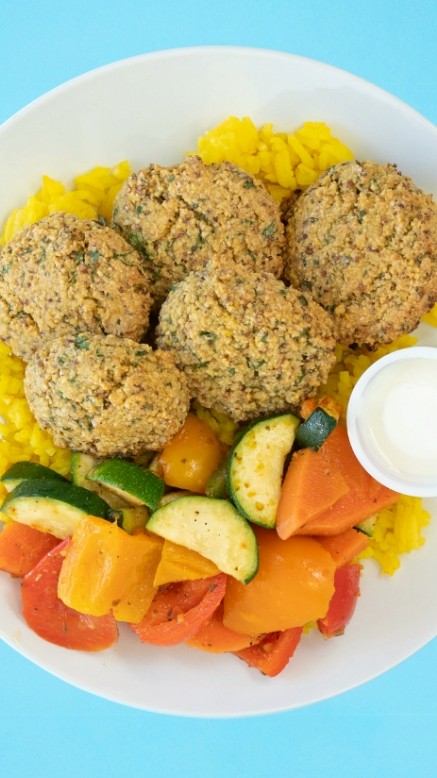 Bowl with falafel, roasted vegetables and rice on a blue background