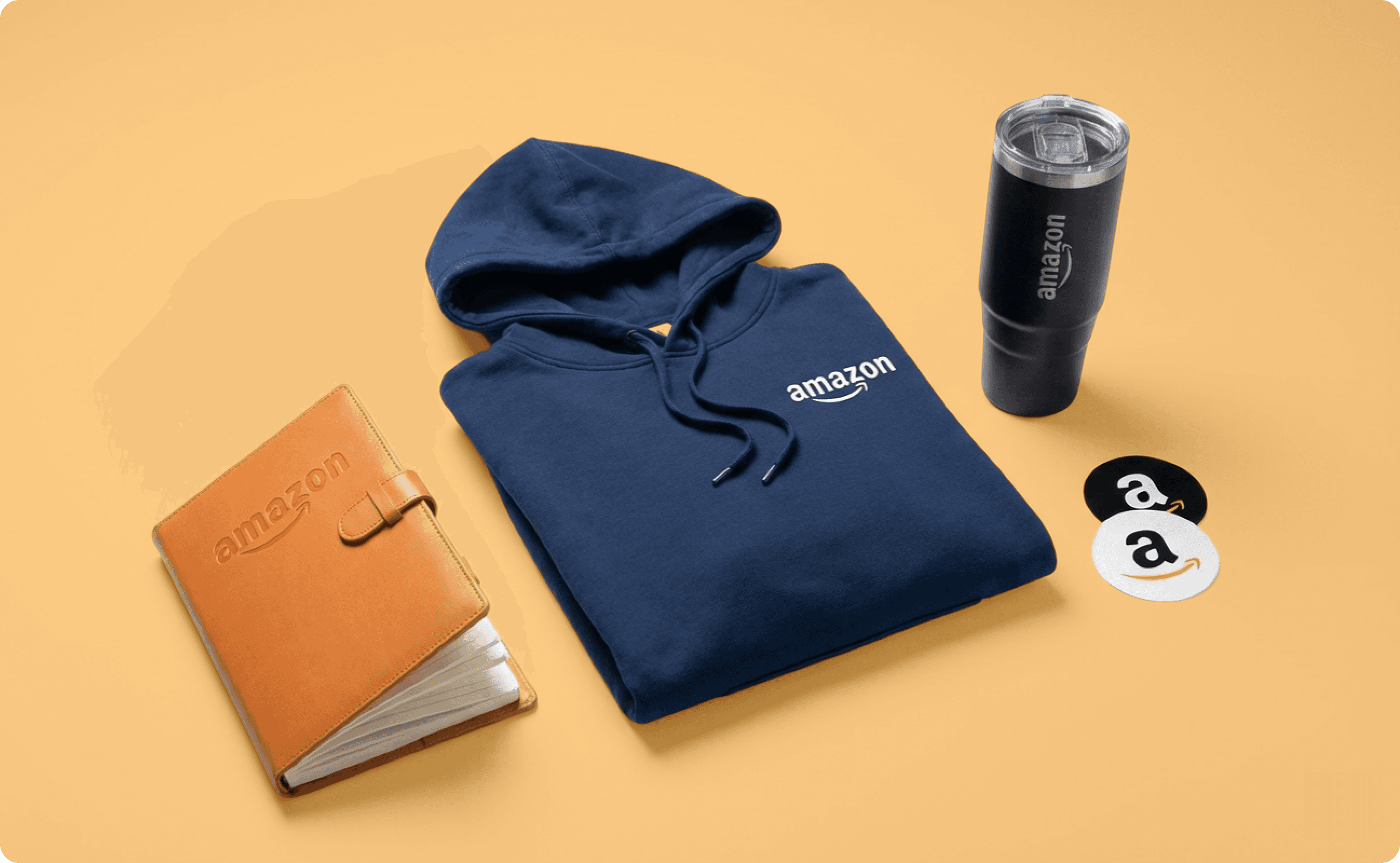 A notebook, a hoodie, a tumbler, and two stickers, all with Amazon logo.