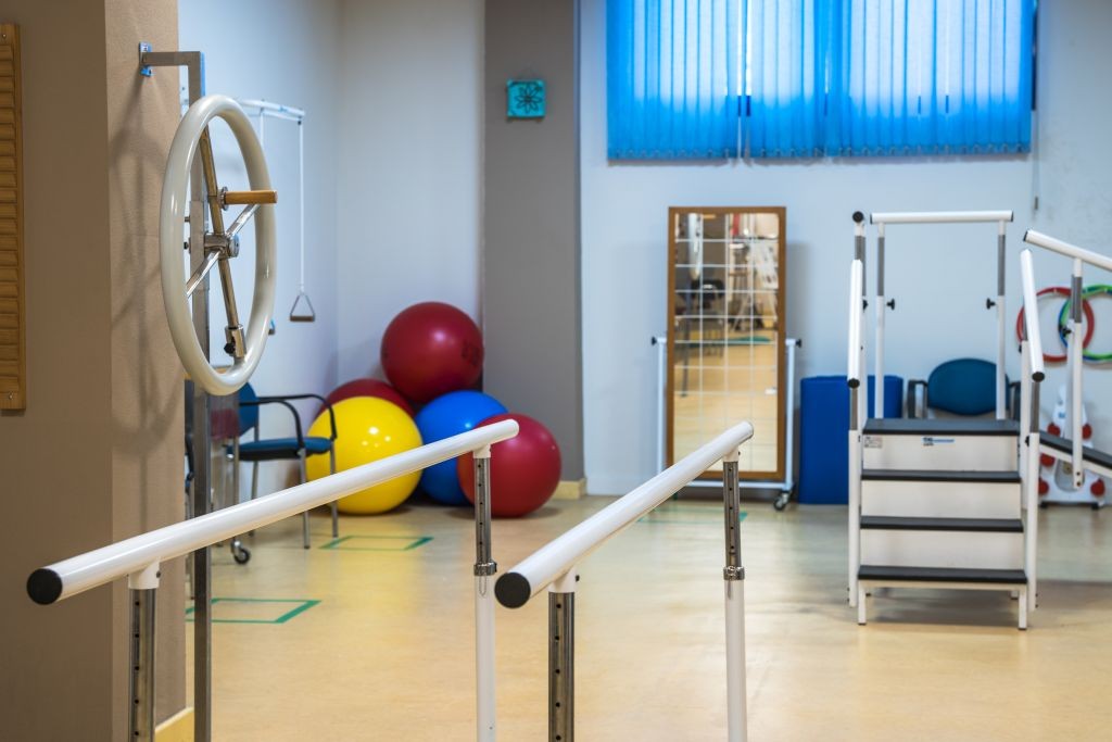 Physiotherapy room equipped with parallel bars, exercise balls, and rehabilitation equipment.