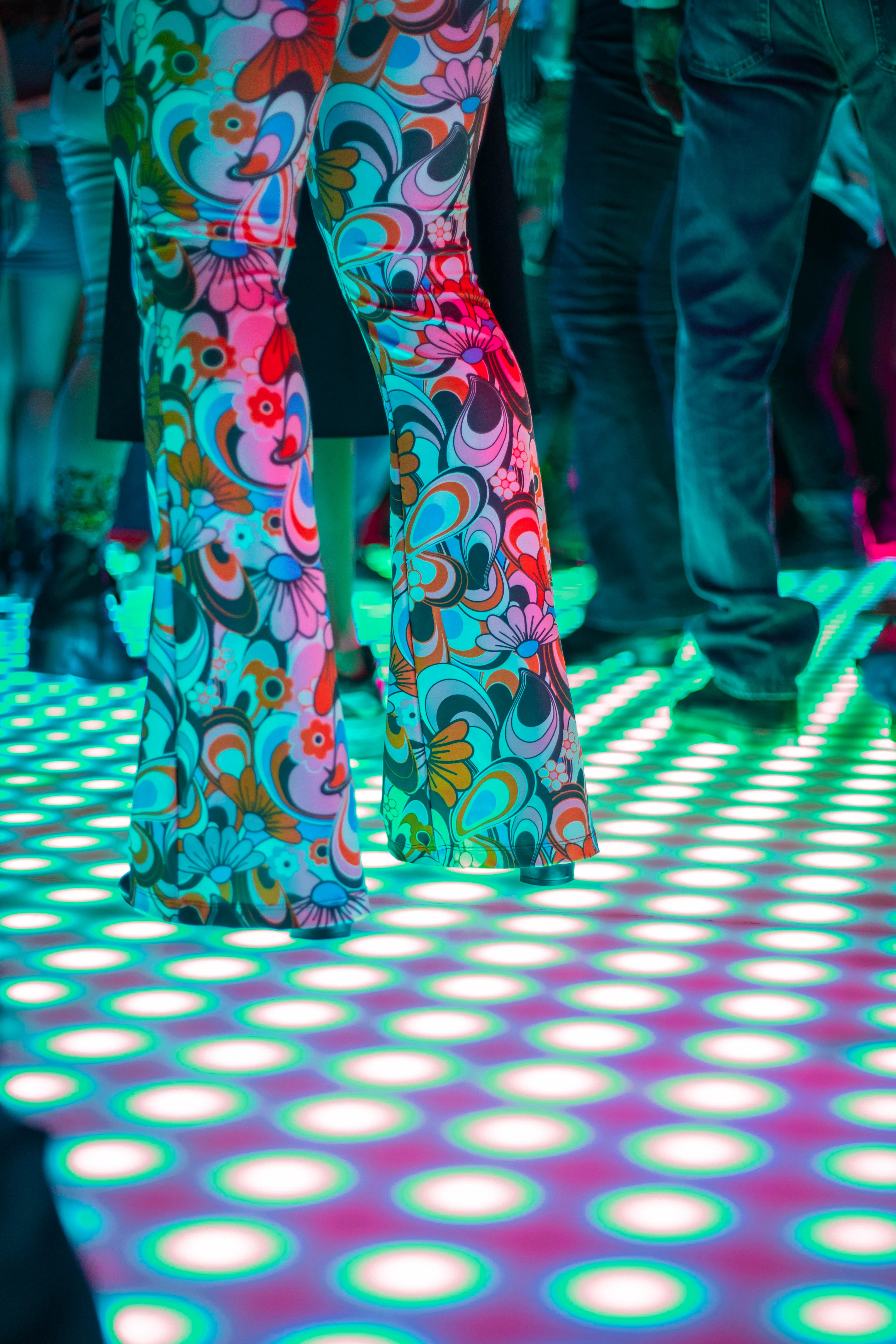 Colorful patterned pants on a dance floor illuminated by vibrant lights, creating a lively atmosphere.
