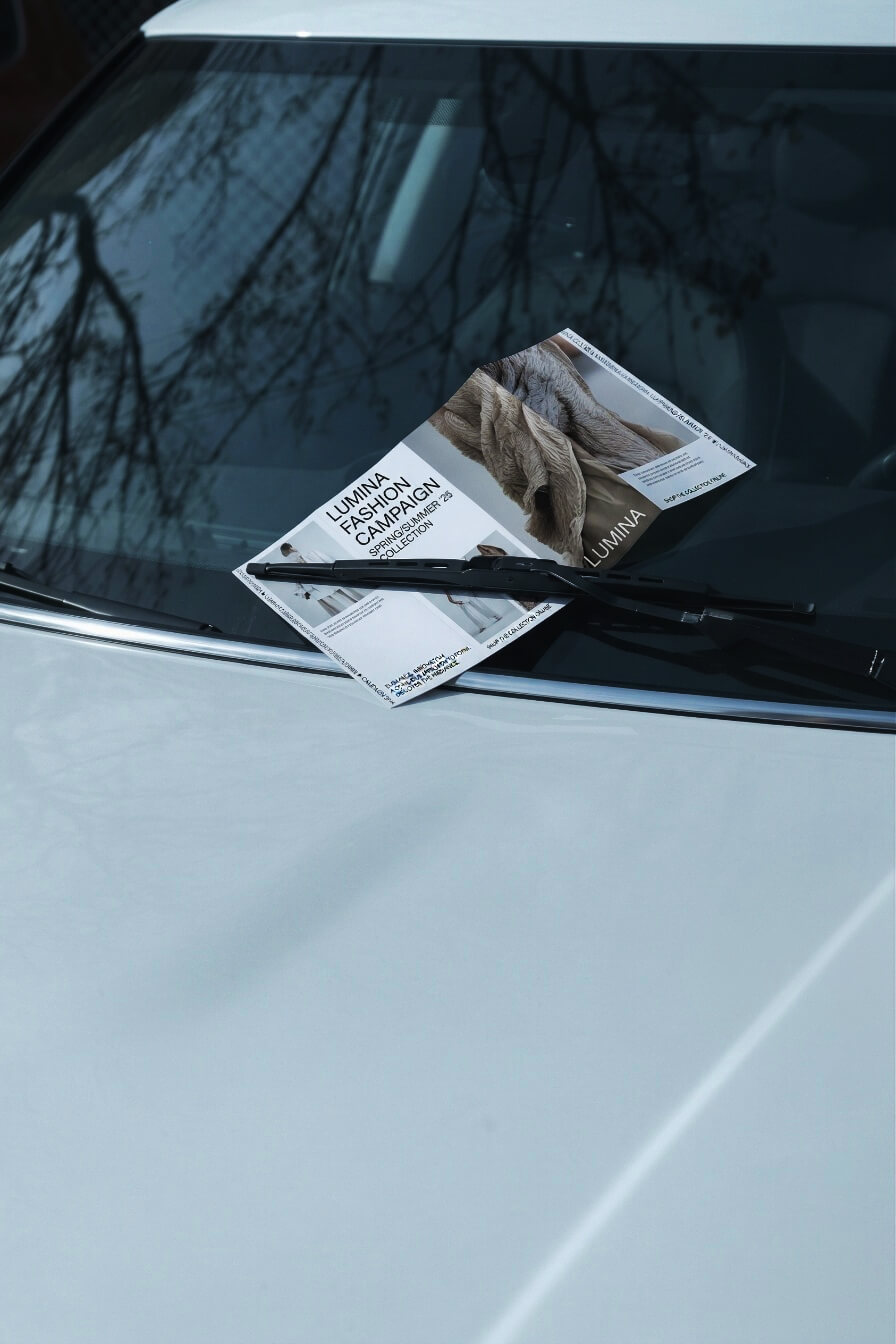 Close-up of a minimalist fashion editorial brochure tucked under a car's windshield wiper.