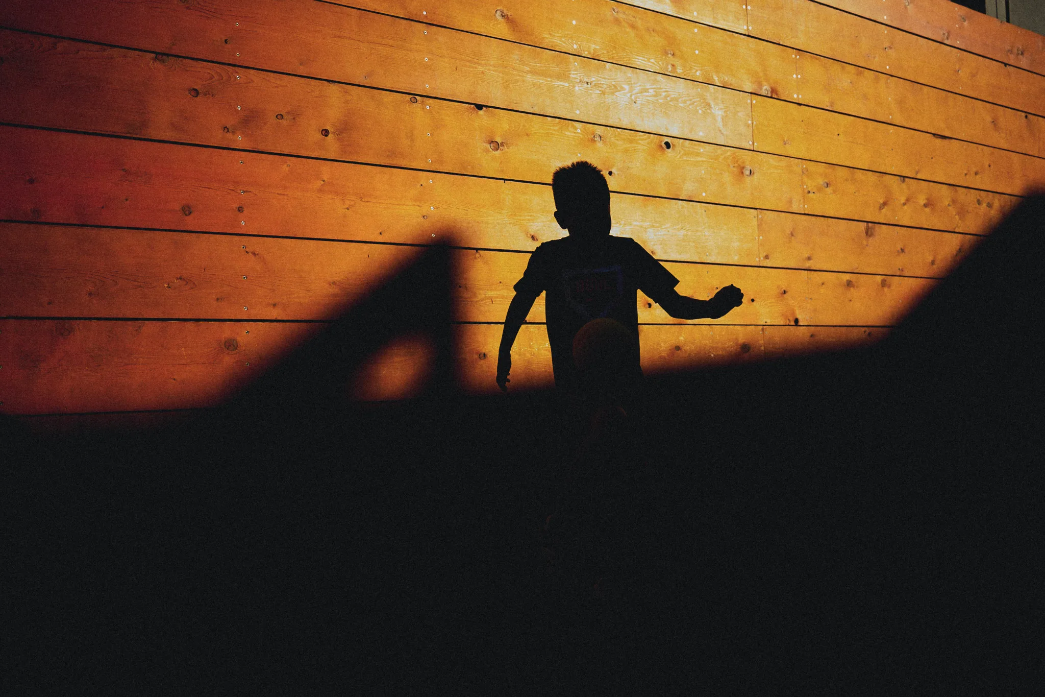 boy silhouetted against wooden wall — lifestyle photography by Tom Kubik